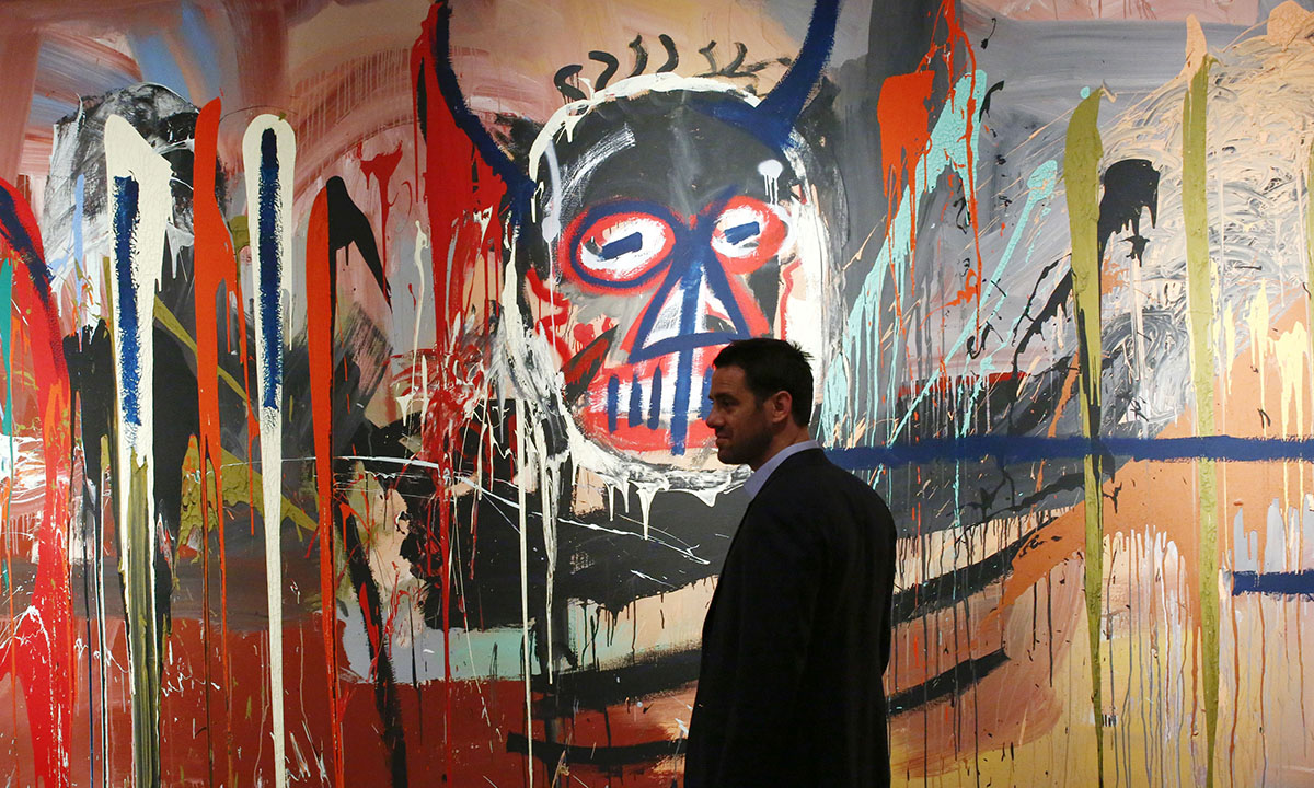man stands next to the artwork 'Untitled' made by artist Jean-Michel Basquiat