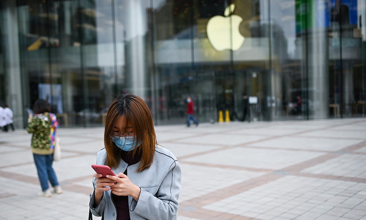 A woman wearing a face mask looks at her mobile phone outside an Apple Store in Beijing