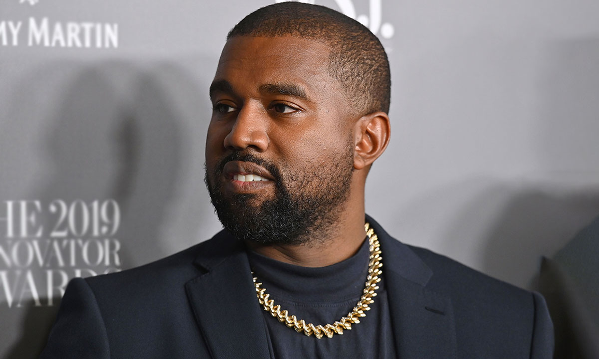 Kanye West black suit gold chain grey background