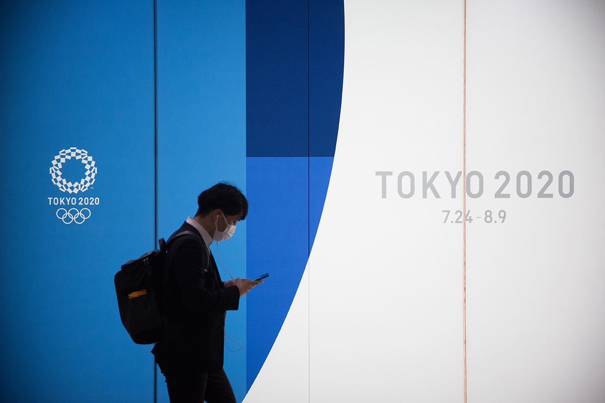 Man wearing face mask walks past billboard for Tokyo olympics