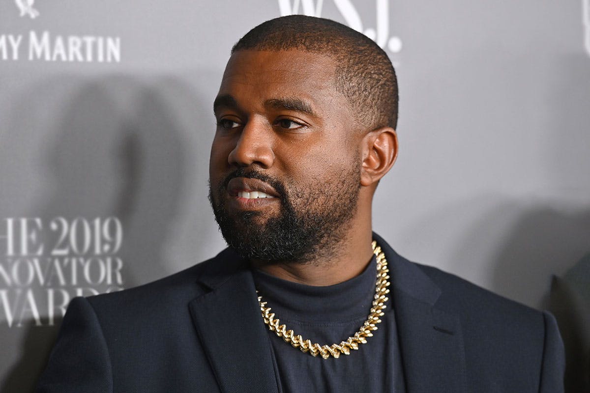 Kanye West black suit gold chain grey background