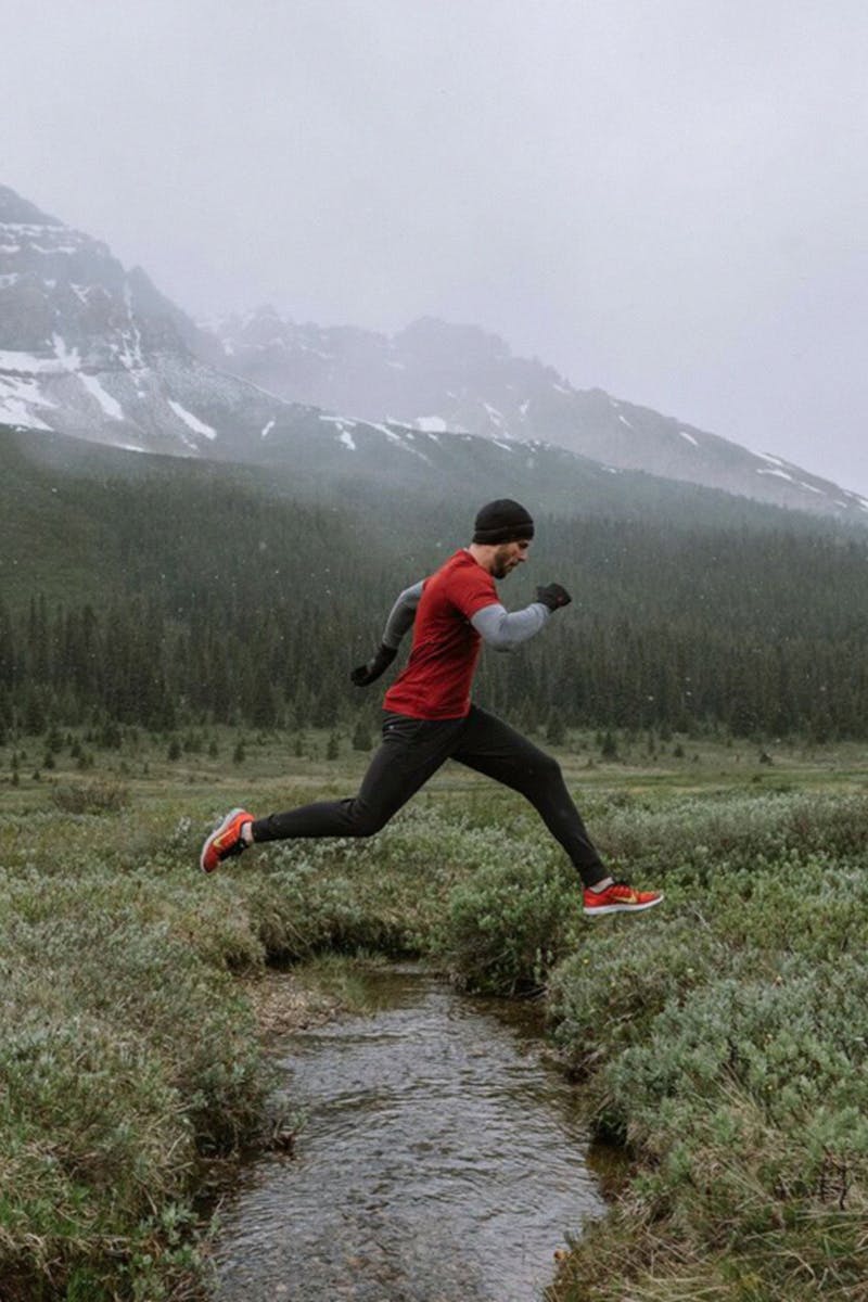 model wearing Rhone outerwear running set while running in mountains