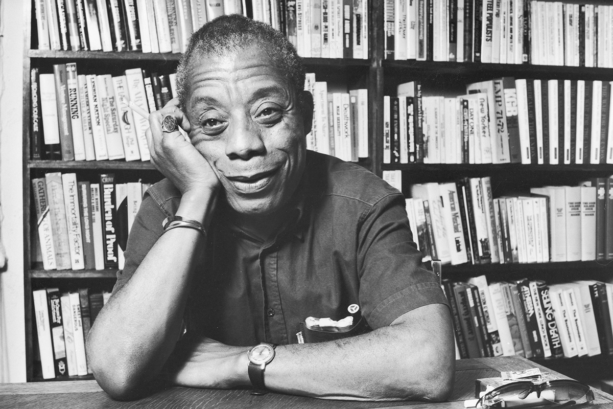 James Baldwin smiling in front of a book shelf