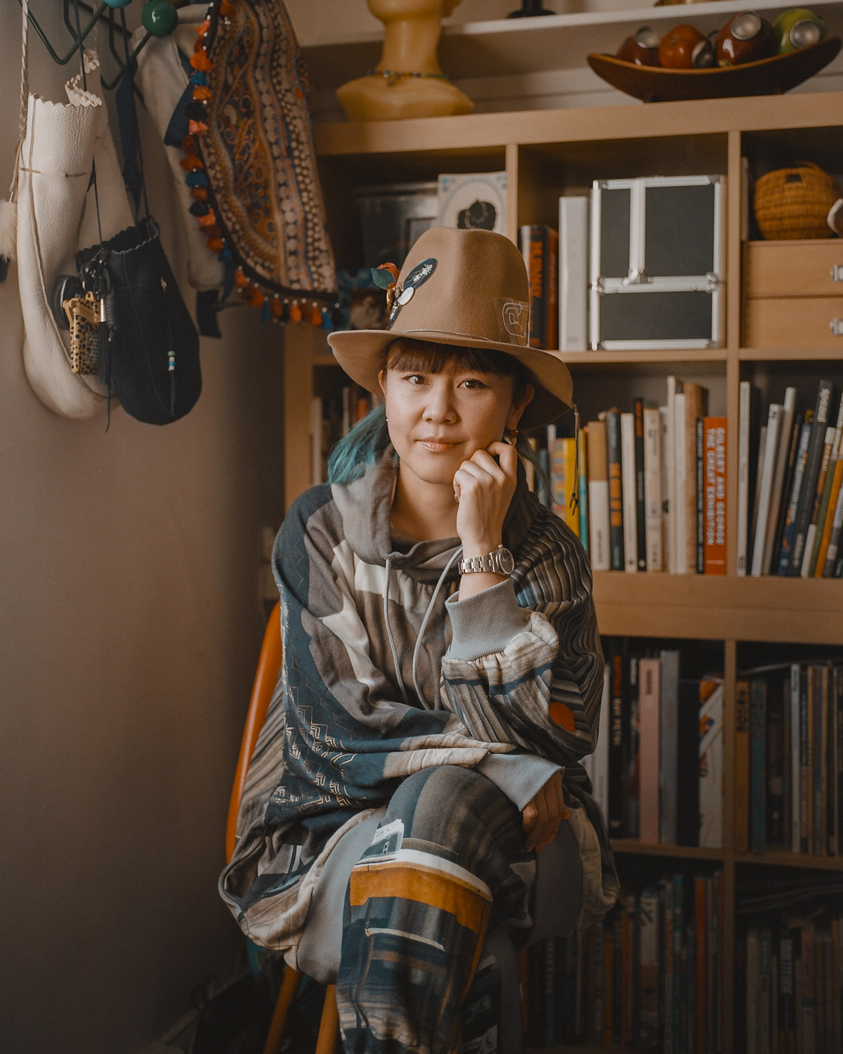 Hitomi Yokoyama wearing a hat sitting indoors in front of a bookshelf