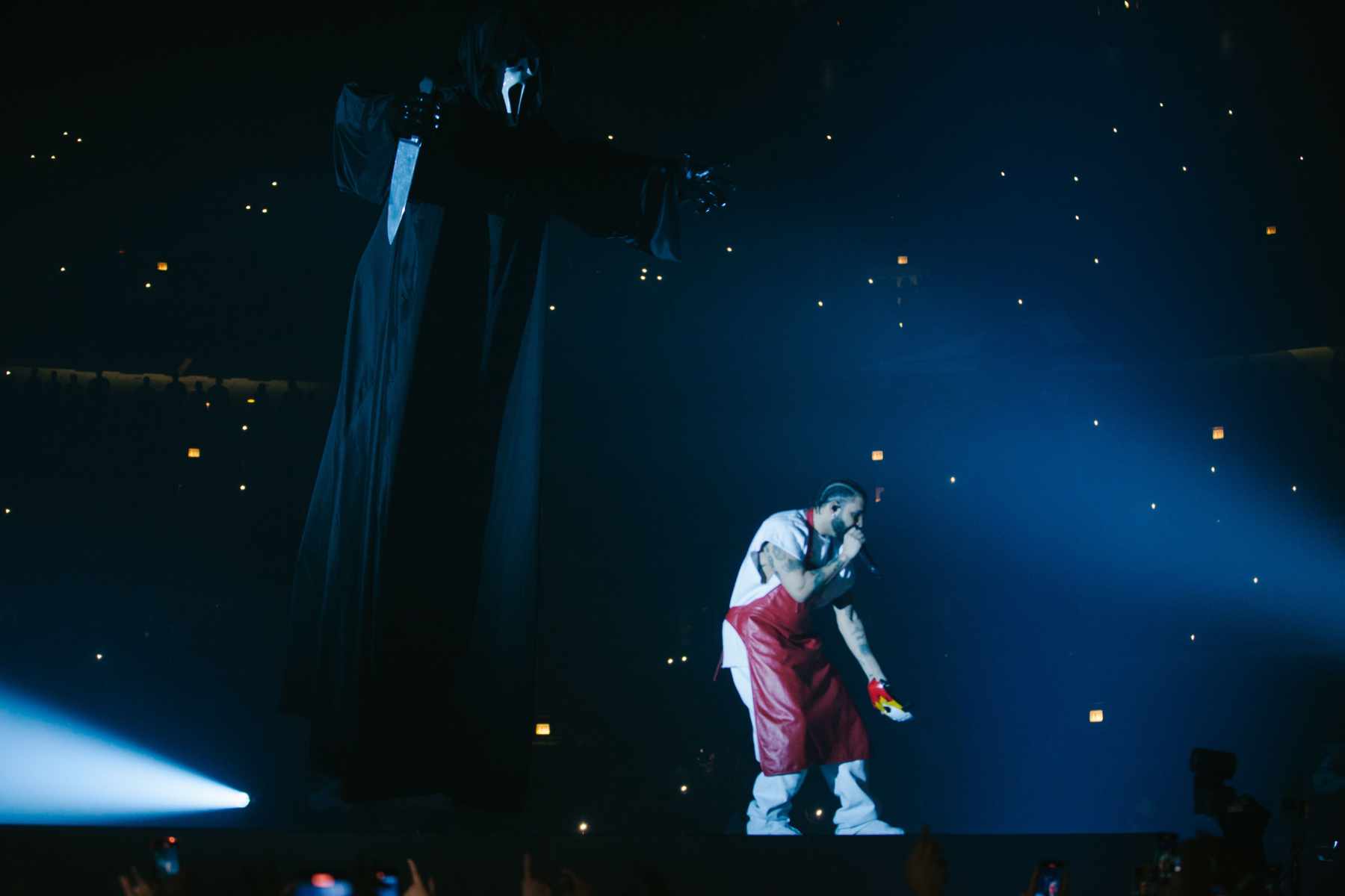 Drake wears a leather apron onstage in front of a grim reaper hologram