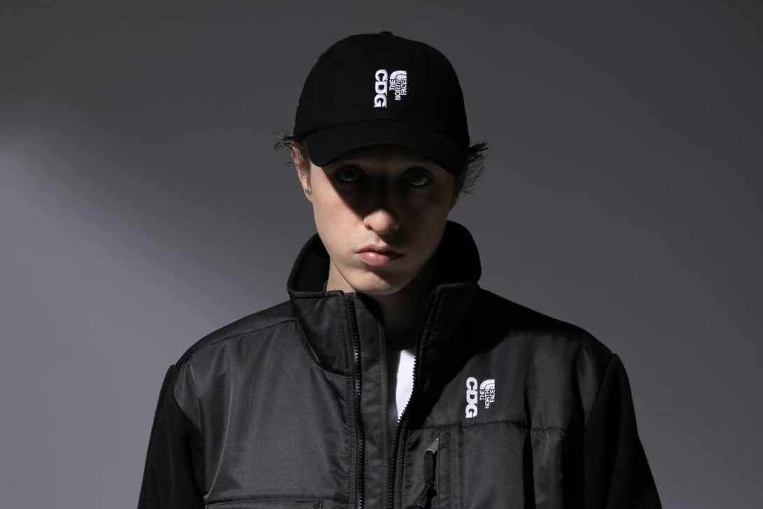 A model wears the CDG x The North Face collaboration, with a black hat & jacket
