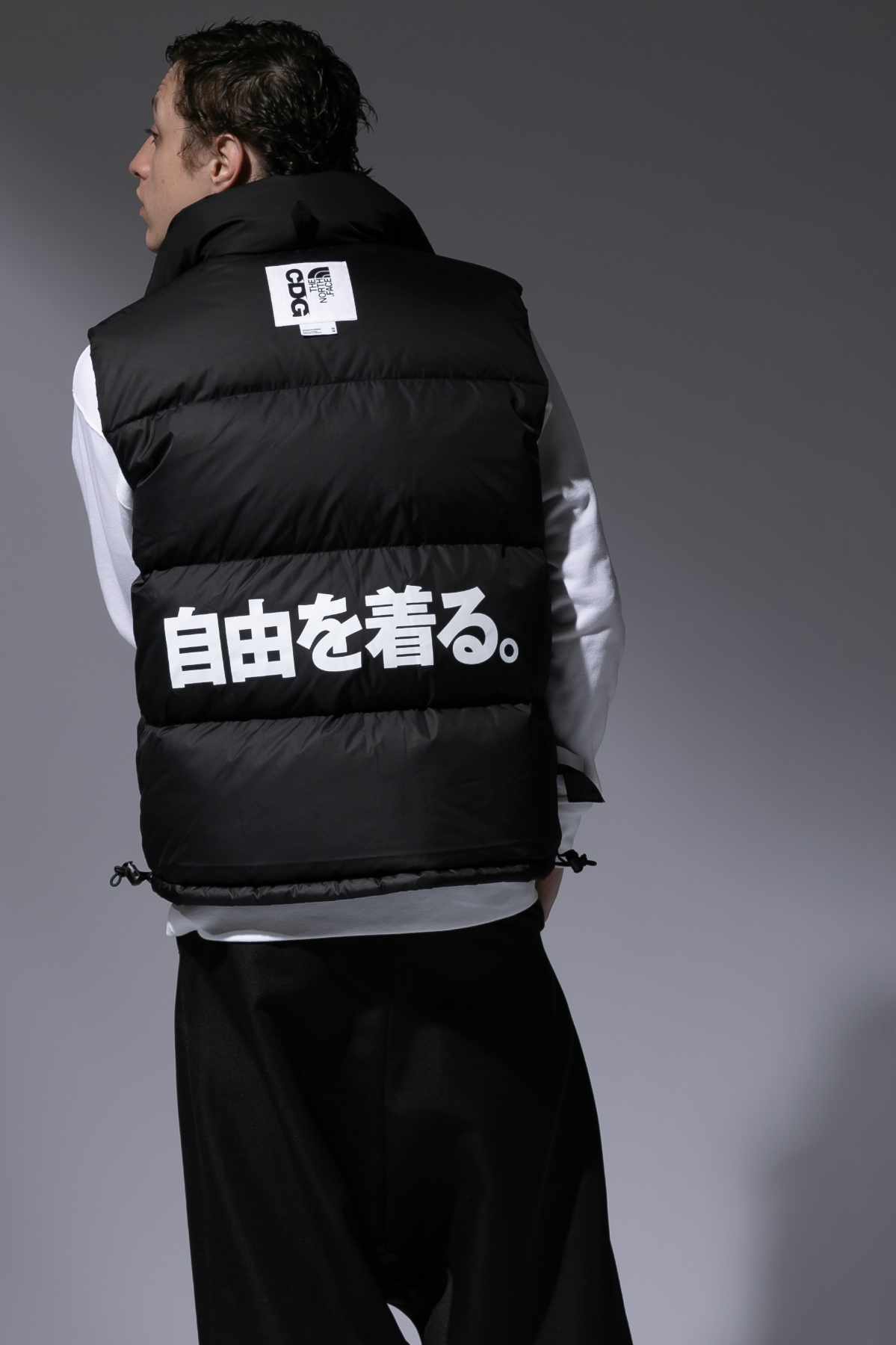 A model wears the CDG x The North Face collaboration, with a black puffer vest