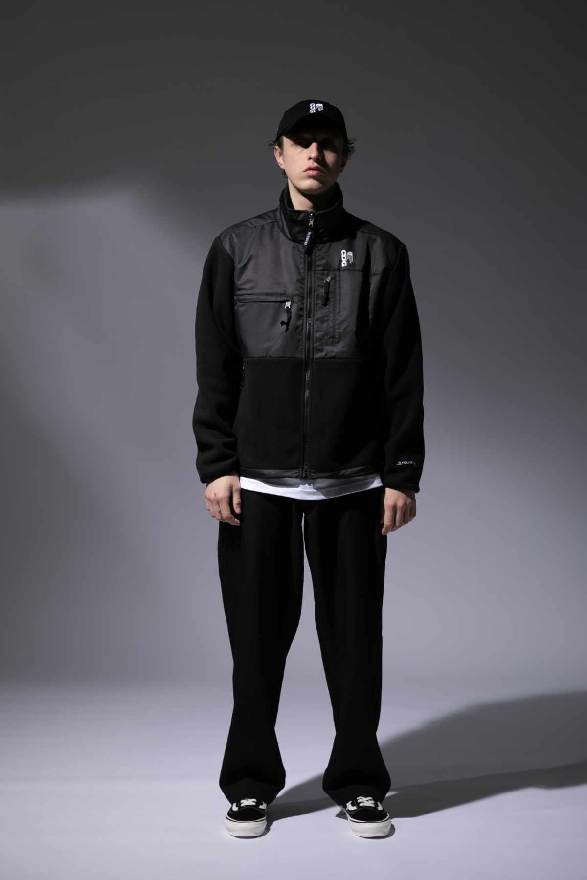 A male model wears the CDG x The North Face collaborative black hat and zip-up jacket