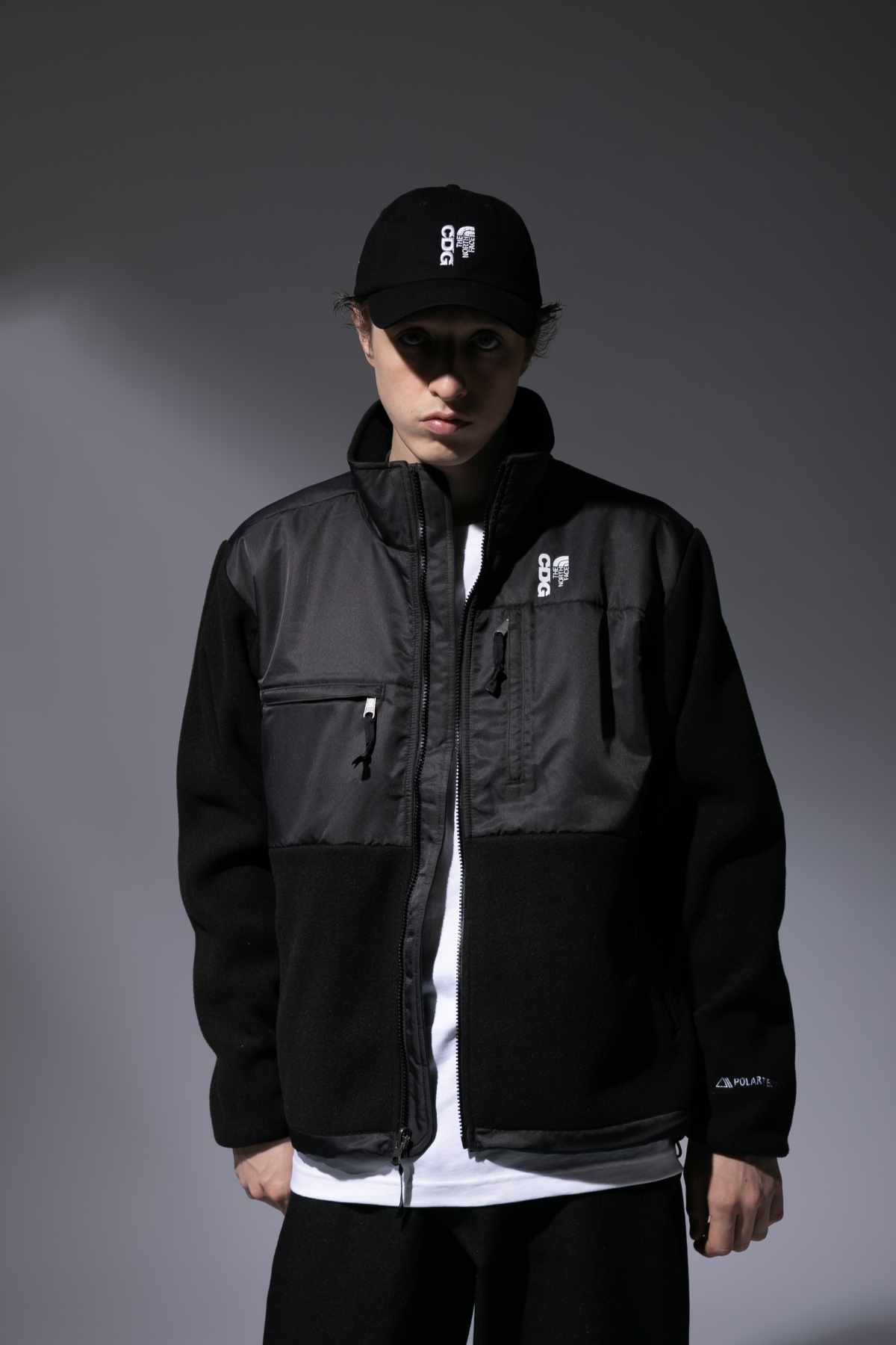 A male model wears the CDG x The North Face collaborative black hat and zip-up jacket