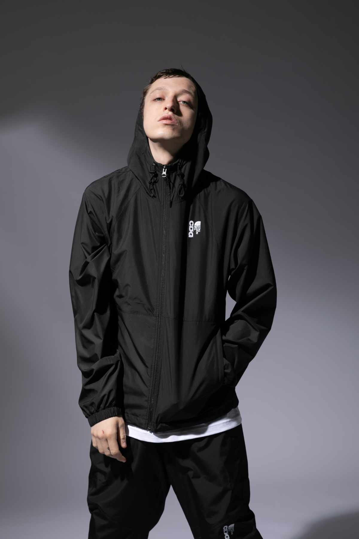 A male model wears the CDG x The North Face collaborative black hooded zip-up jacket