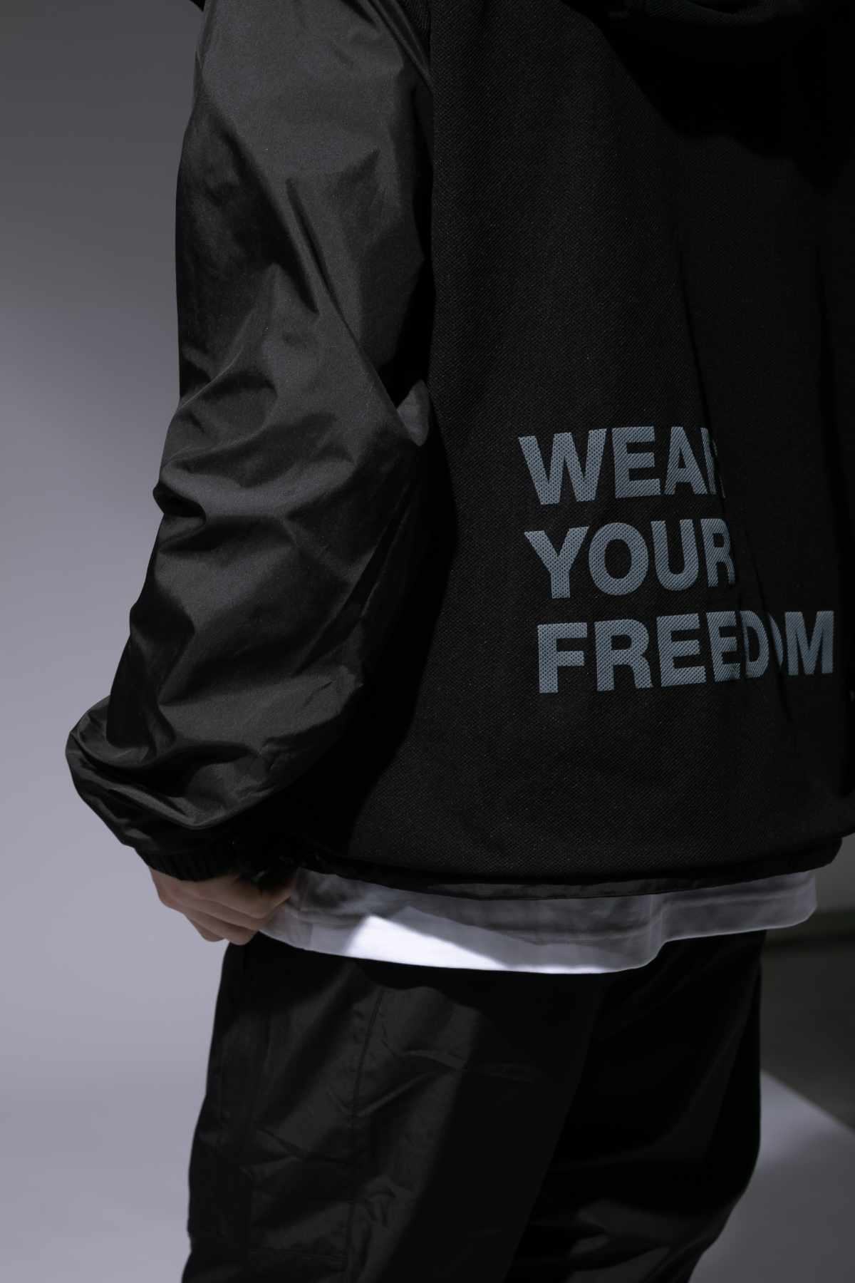 A male model wears the CDG x The North Face collaborative hooded zip-up jacket with "WEAR YOUR FREEDOM" text