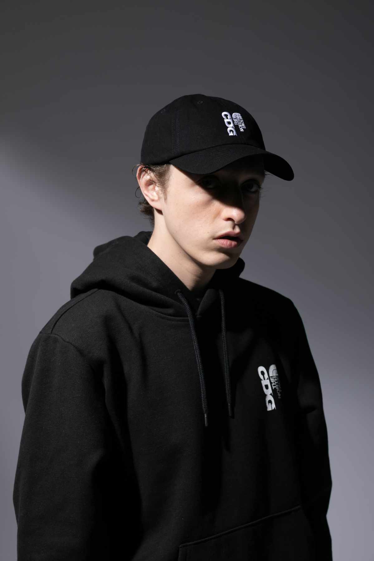 A male model wears the CDG x The North Face collaborative black hat and hoodie sweater
