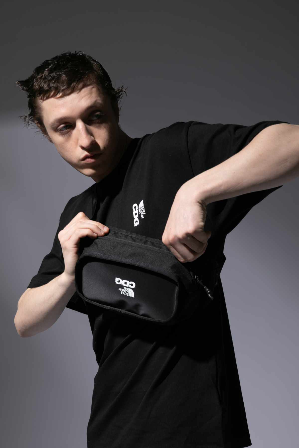 A male model wears the CDG x The North Face collaborative black bag, T-shirt, and matching trousers