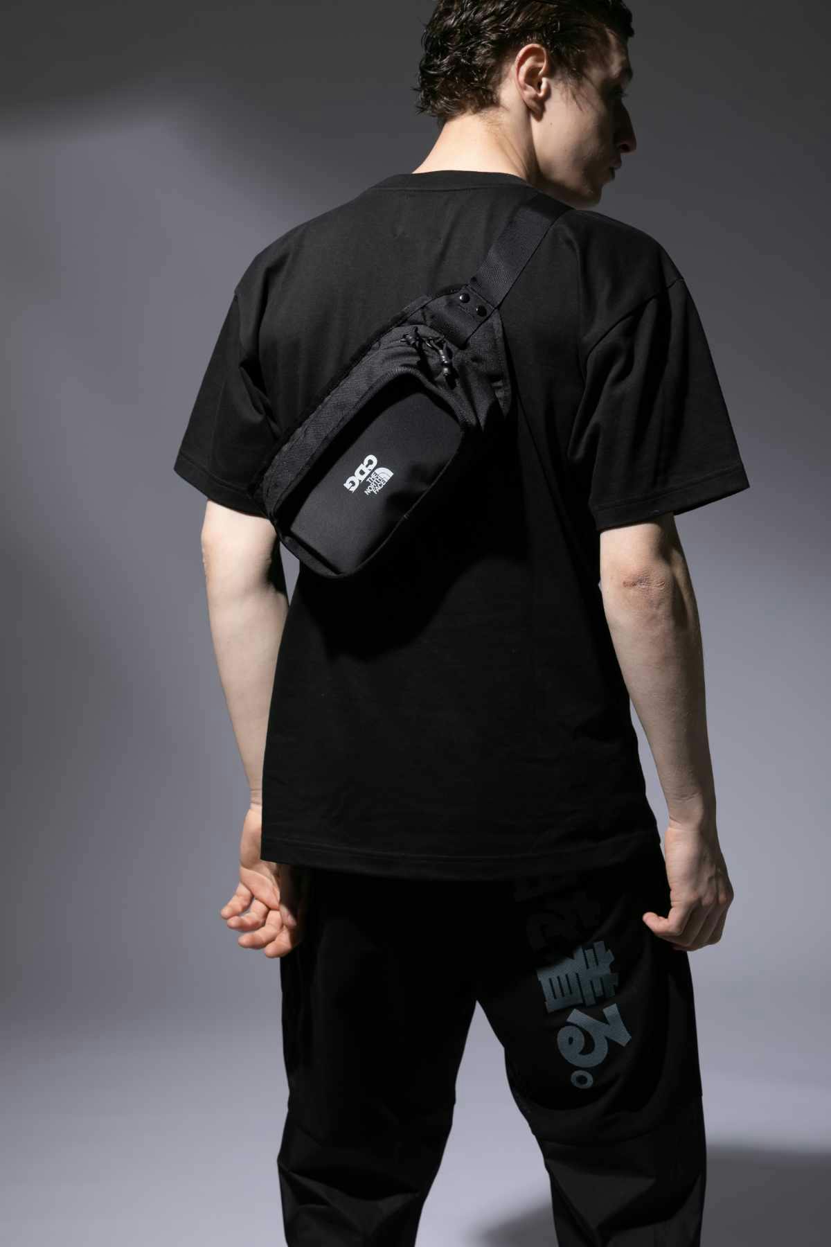 A male model wears the CDG x The North Face collaborative black bag, T-shirt, and matching trousers