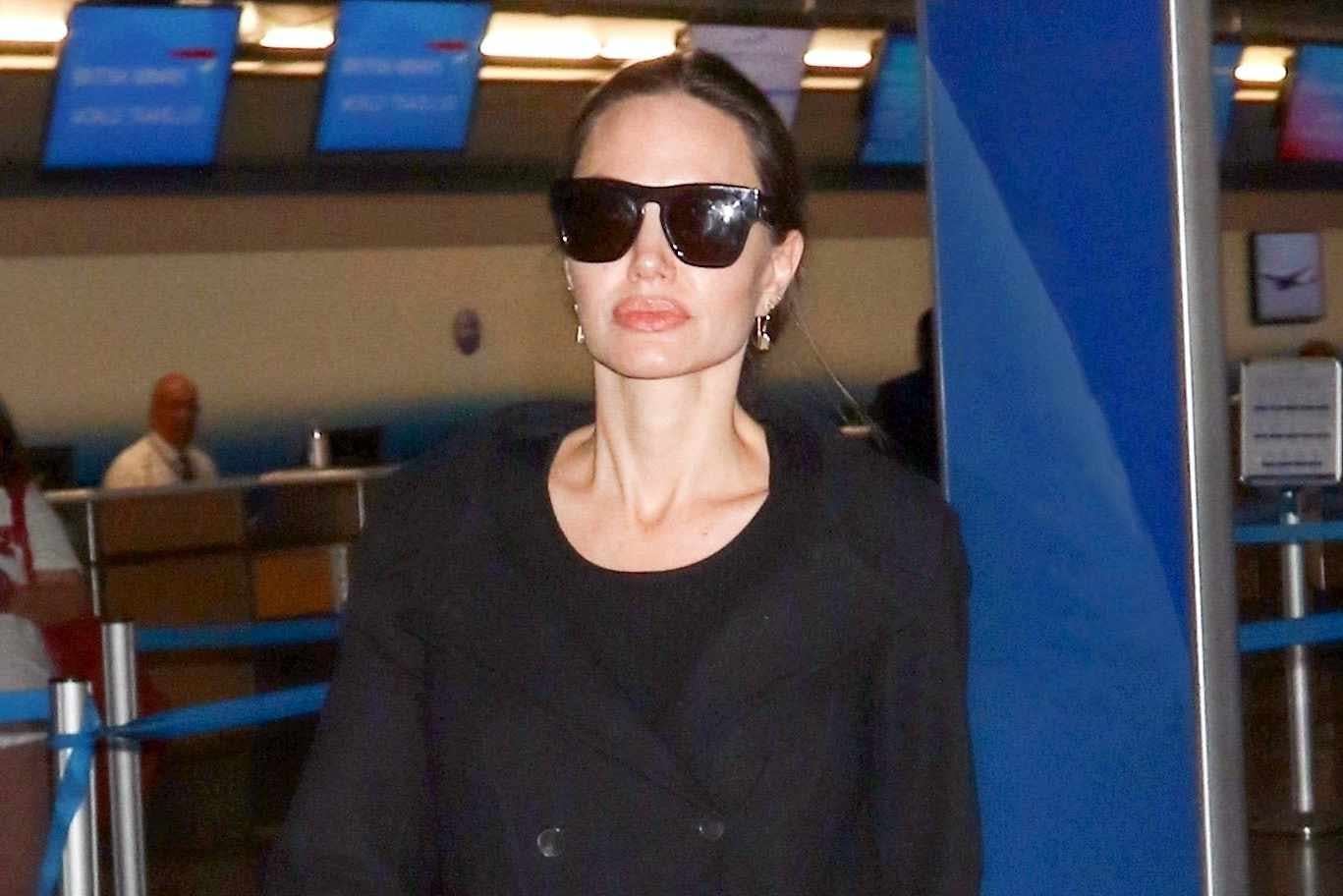 angelina jolie wears a black coat & skirt with CELINE and Louis Vuitton handbags at an airport with her two kids