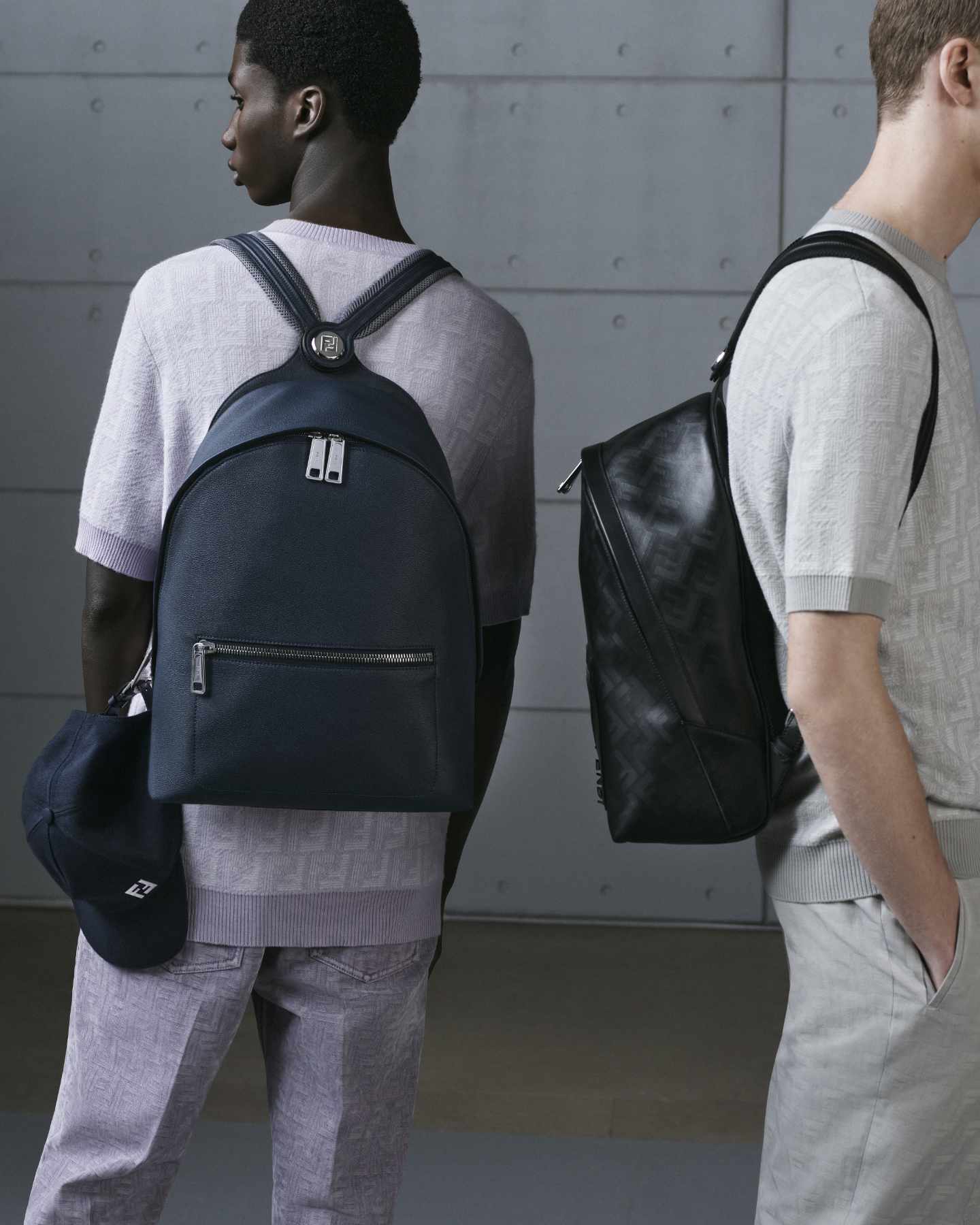 Two models wear Fendi's Chiodo Backpack in navy grain leather and black monogram