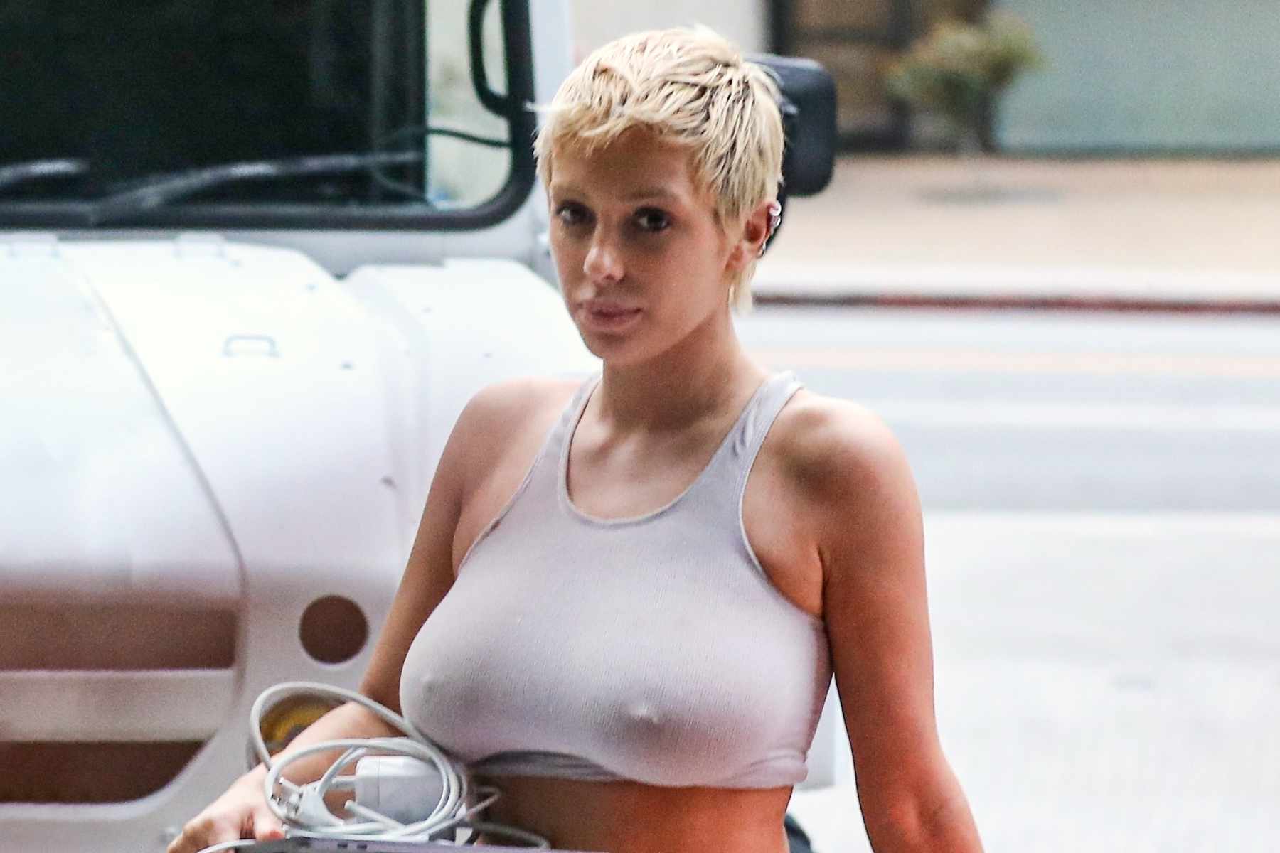 Bianca Censori, Kanye West's wife, is seen wearing a see-through sportsbra & leggings with short blond hair while holding a Macbook