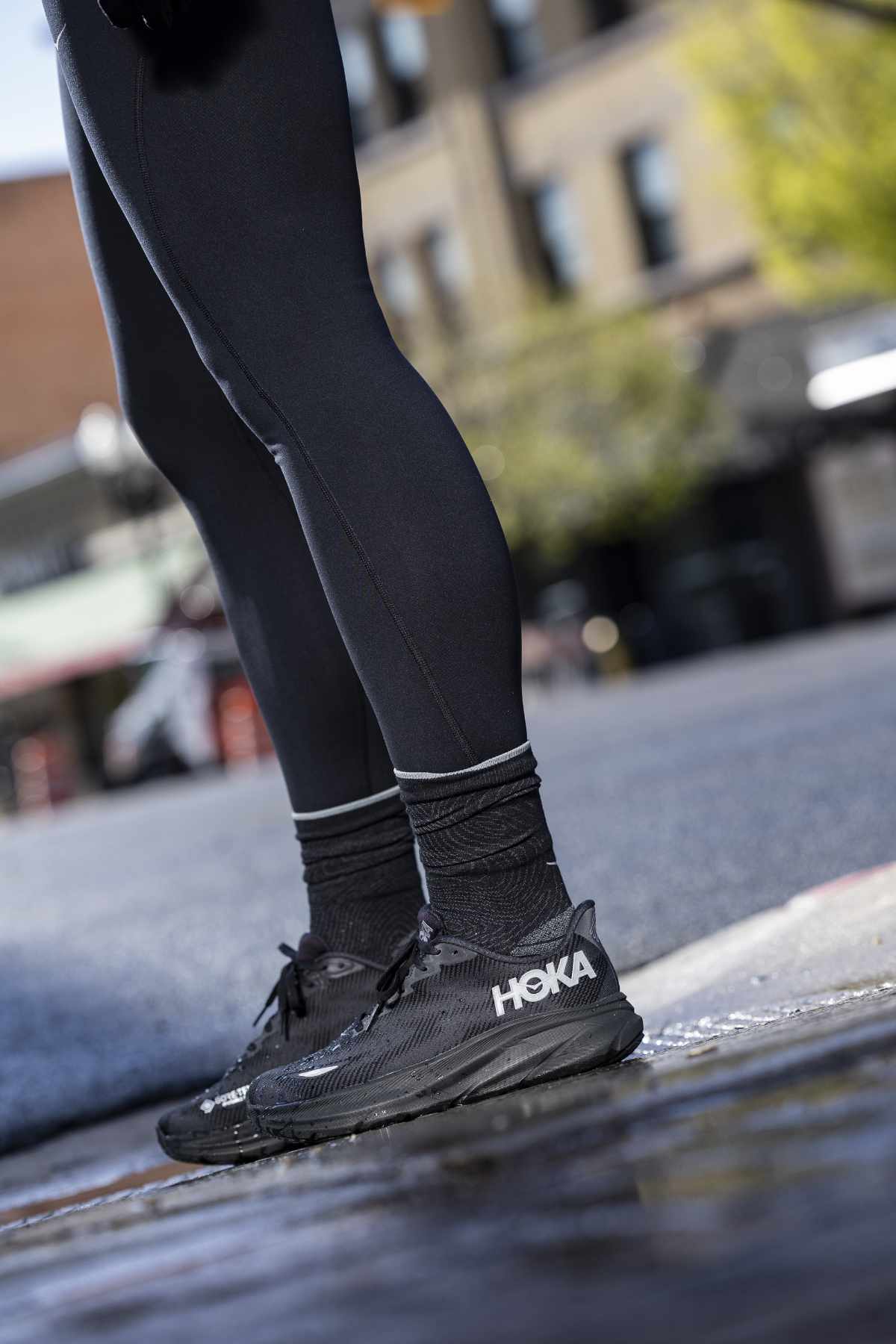 The legs of a runner wearing HOKA's Clifton 9 sneaker in a black GORE-TEX-lined colorway