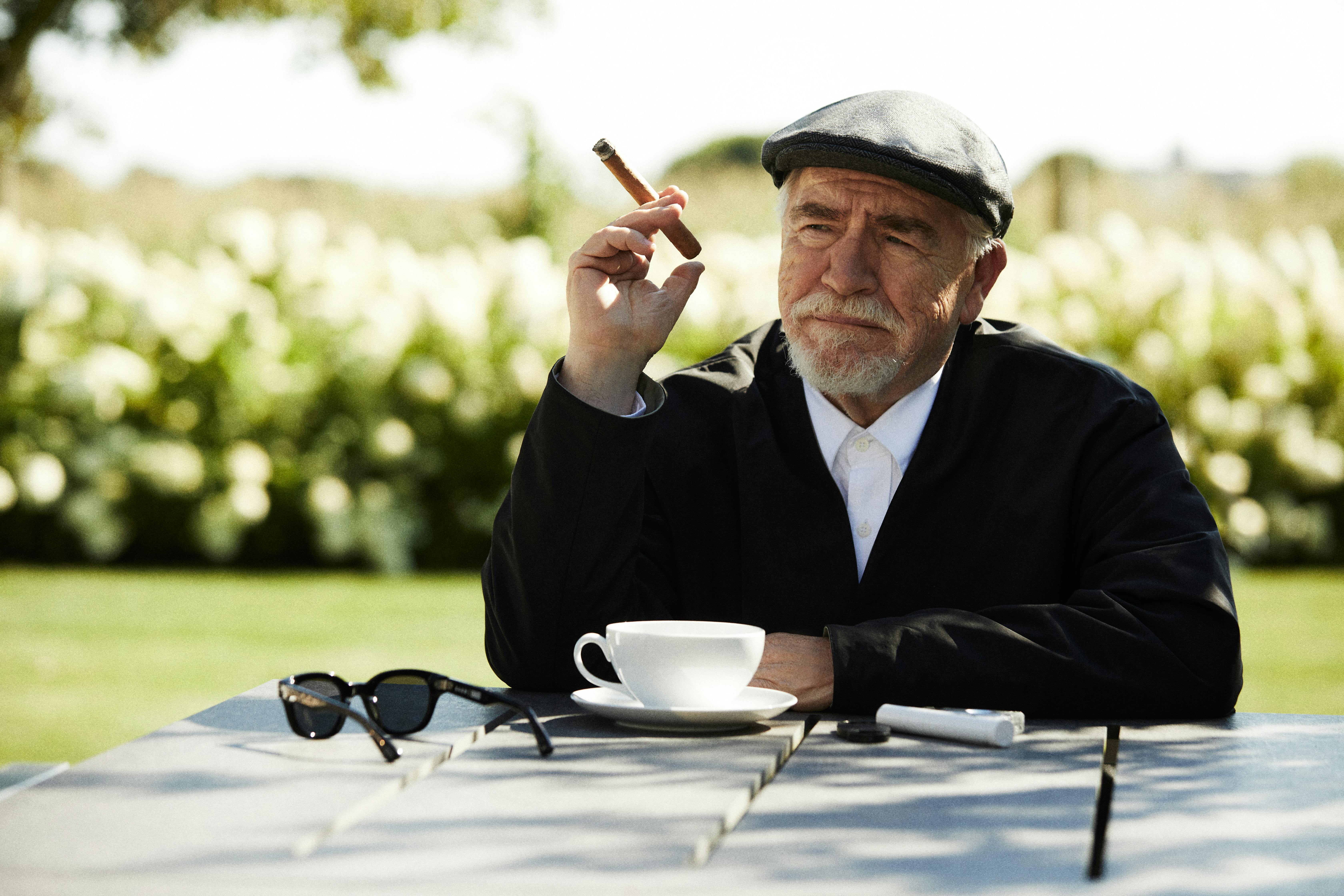 A photograph of Brian Cox, the actor famous for portraying Logan Roy on 'Succession,' wears a KITH blazer and shirt while holding a cigar