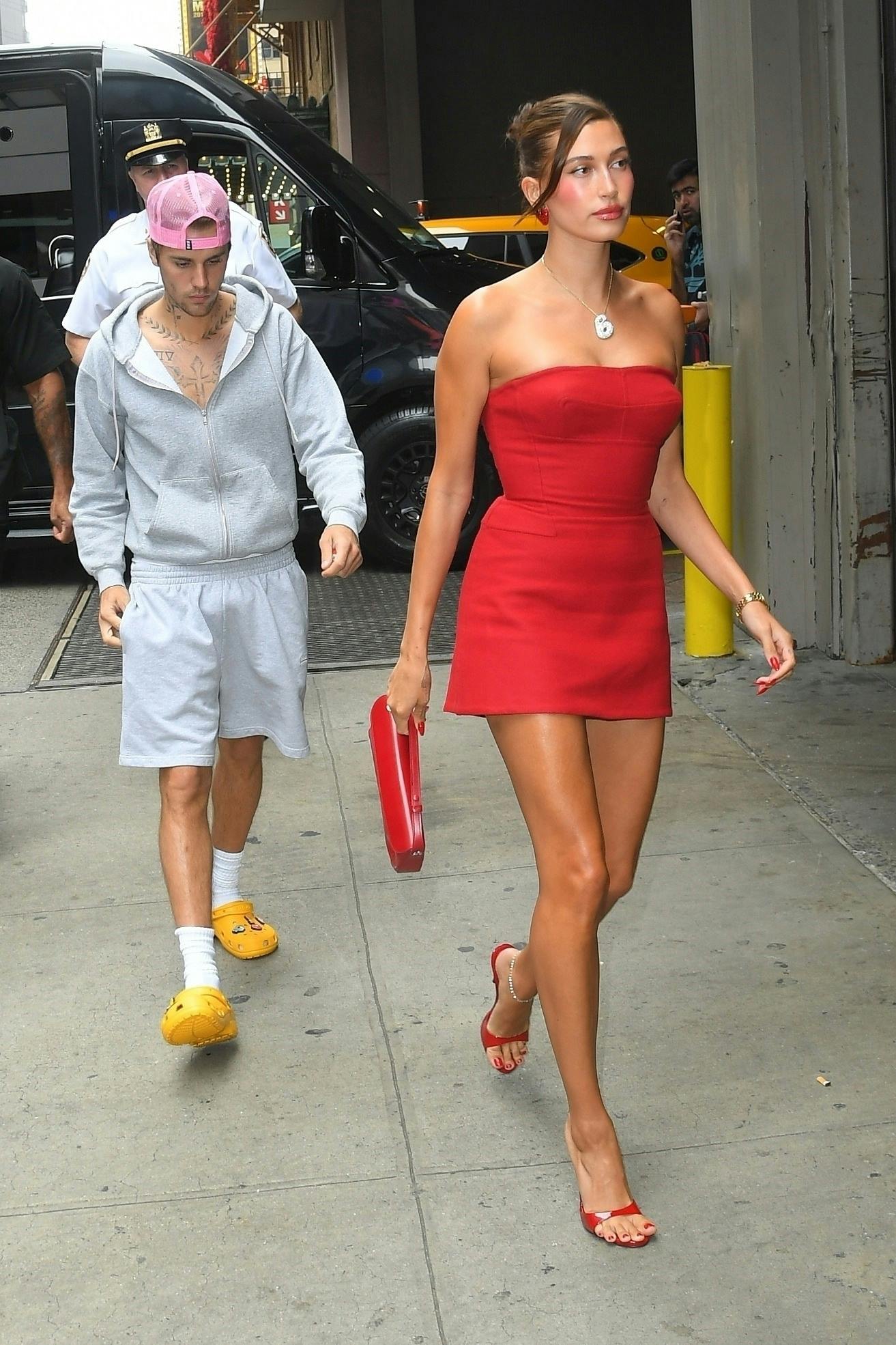 Justin Bieber seen wearing a grey hoodie & sweat shorts with Crocs while Hailey Bieber wears a little red dress with matching heels & handbag