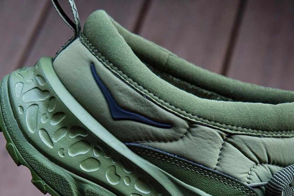 An in-hand photograph of a beige HOKA ONE ONE mule sneaker with a chunky sole and backless design