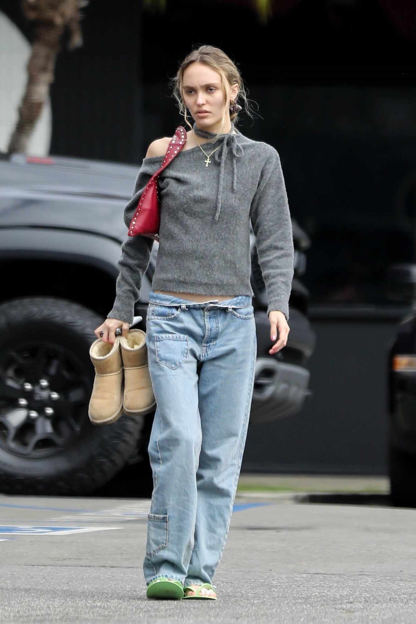 Lily-Rose Depp wears a cross necklace, grey knit top, red handbag, baggy jeans & UGG boots with yellow flip-flops on October 2 in Los Angeles