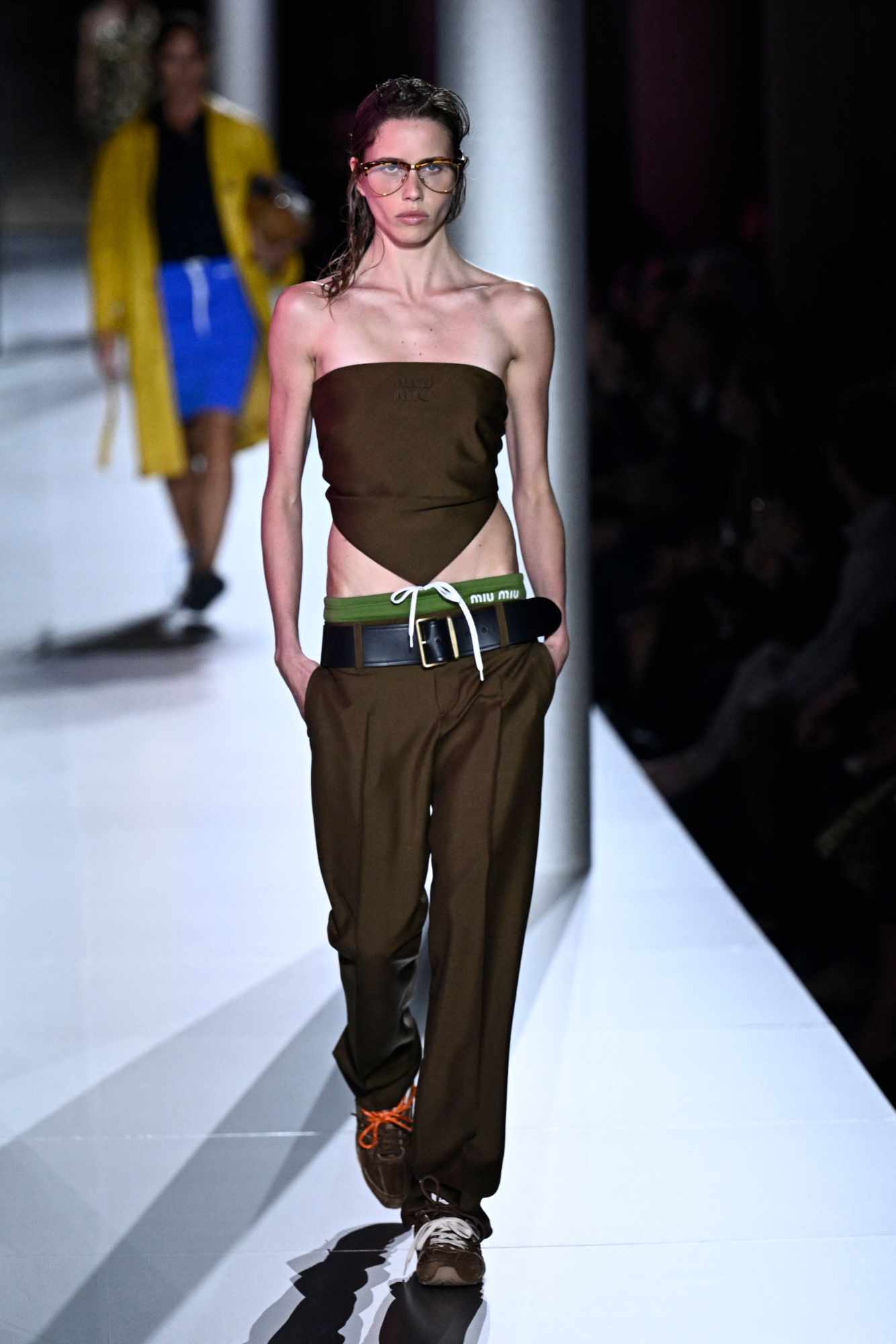 A model wears a brown Miu Miu top, matching slacks, and the latest Miu Miu x New Balance 530 sneaker collab on the SS24 runway in Paris