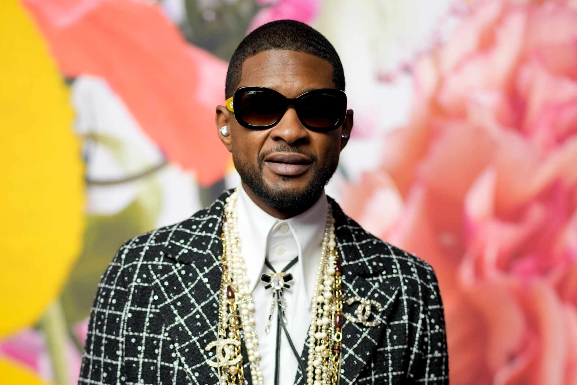 Usher wears sunglasses & grey tweed Chanel outfit with pearls at Paris Fashion Week on October 3, 2023