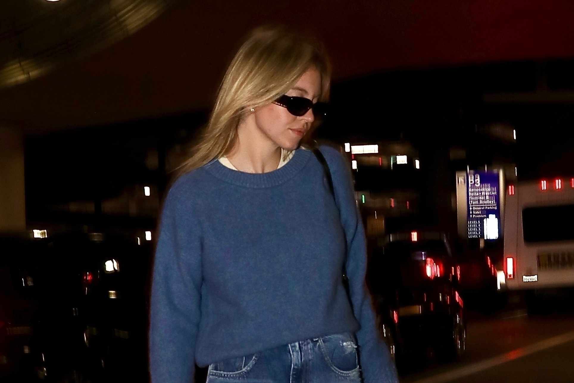 Sydney Sweeney wears Prada sunglasses, a baggy navy sweater, straight leg jeans, and black leather boots out in Los Angeles
