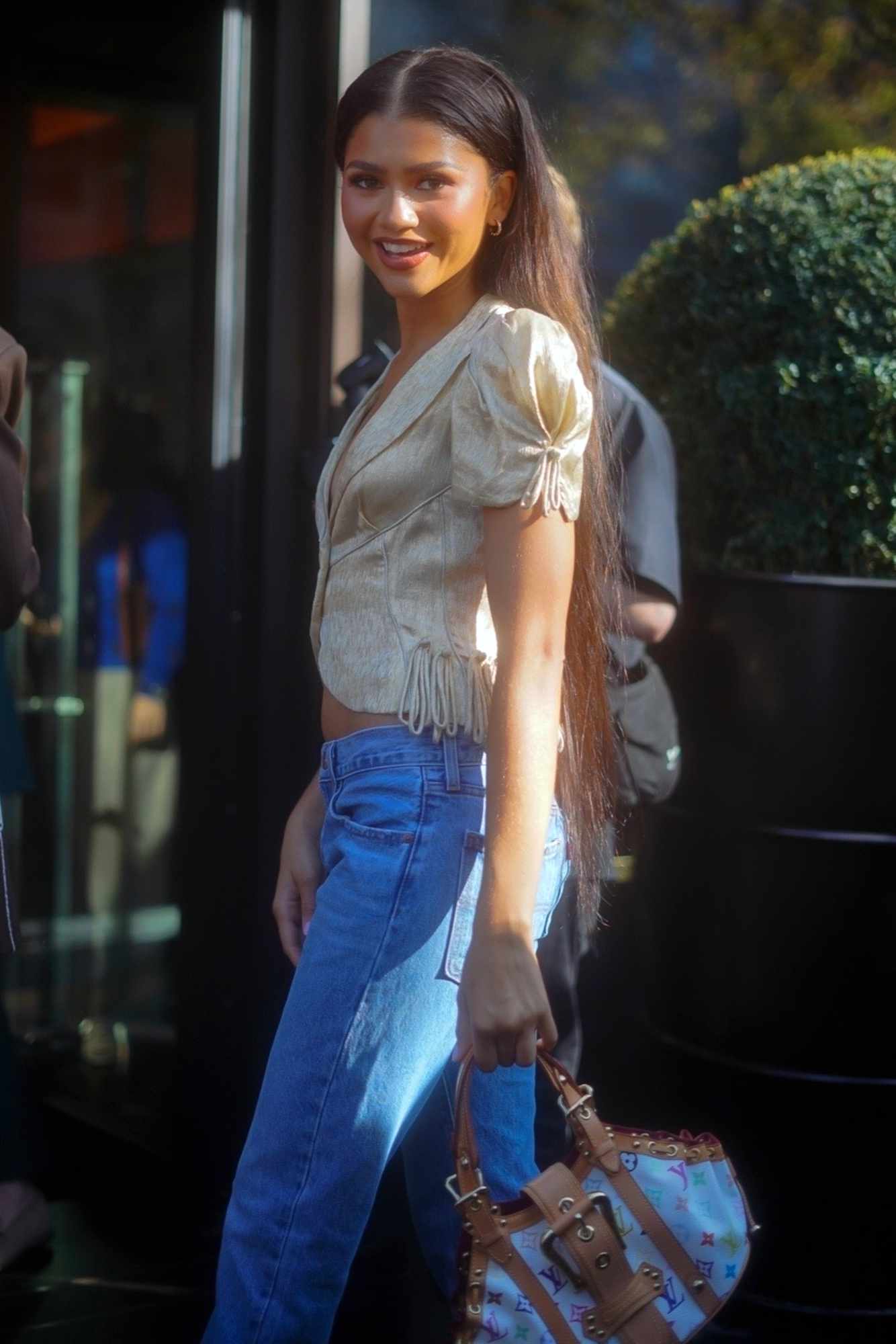 Zendaya wears a shiny pink blouse, blue denim jeans & a Louis Vuitton bag at Paris Fashion Week