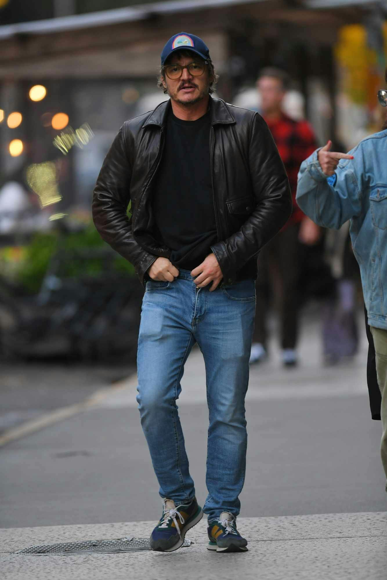 Pedro Pascal is seen wearing a baseball hat, oversized glasses, leather jacket, black T-shirt, washed out denim jeans & New Balance 237 sneakers