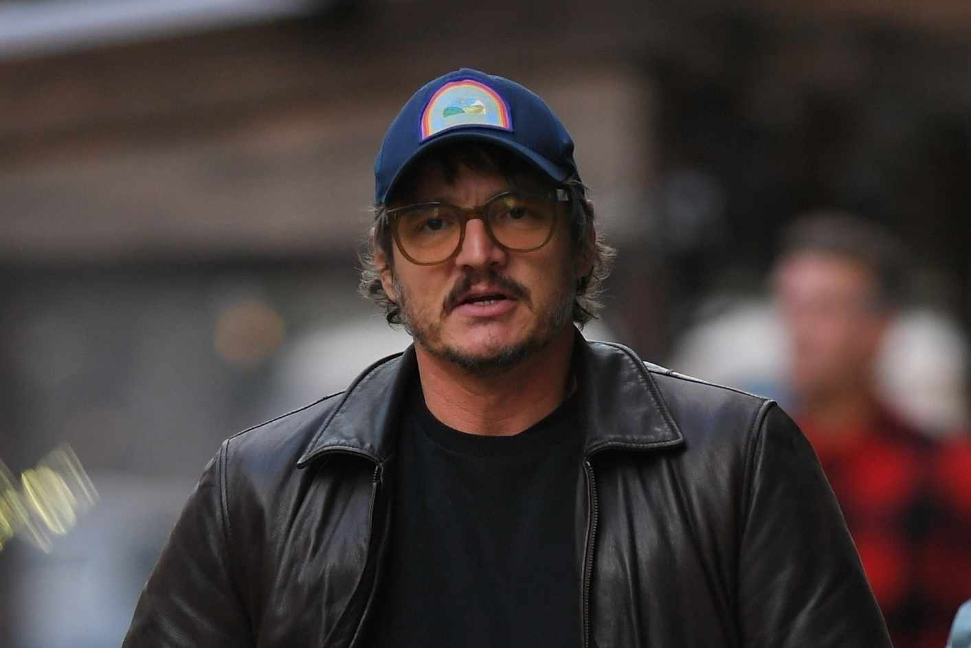 Pedro Pascal is seen wearing a baseball hat, oversized glasses, leather jacket, black T-shirt, washed out denim jeans & New Balance 237 sneakers