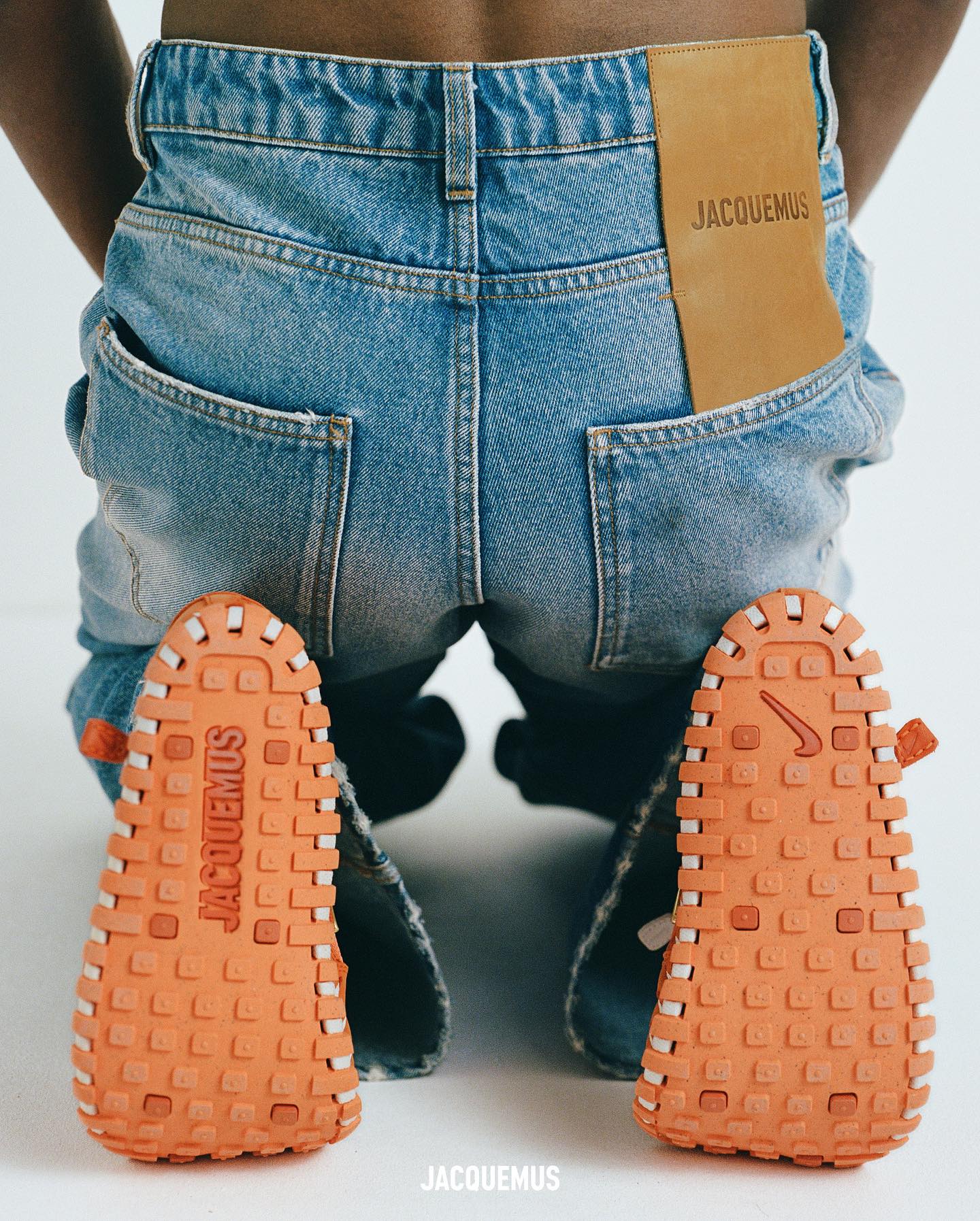 A model wears Jacquemus x Nike JF1 sneaker & merch in orange colorways