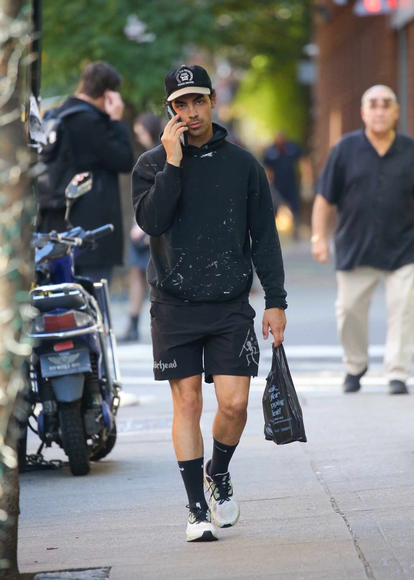 Joe Jonas is seen in New York wearing a dad cap, painted hoodie, Motorhead shorts & running sneakers with black socks