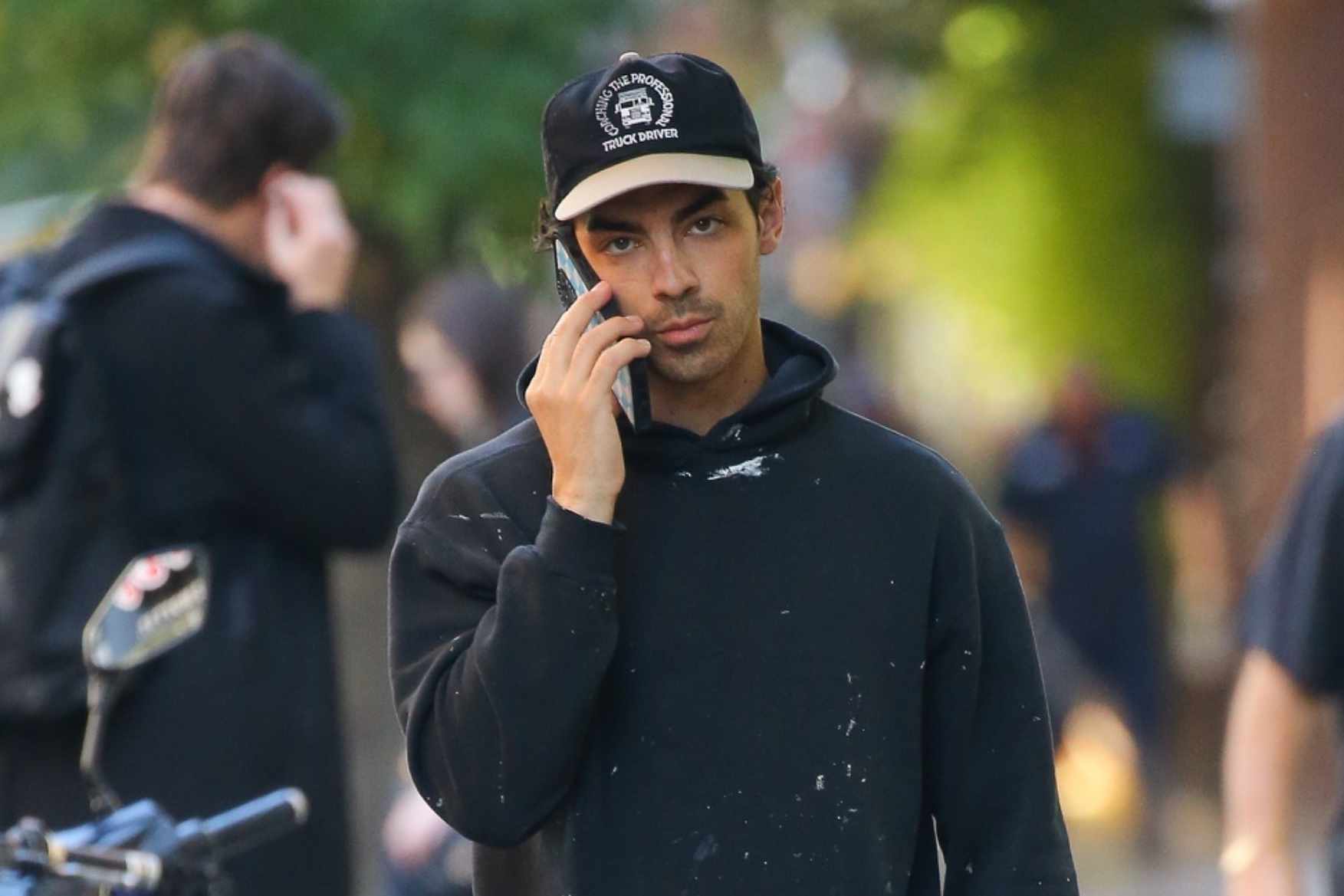 Joe Jonas is seen in New York wearing a dad cap, painted hoodie, Motorhead shorts & running sneakers with black socks
