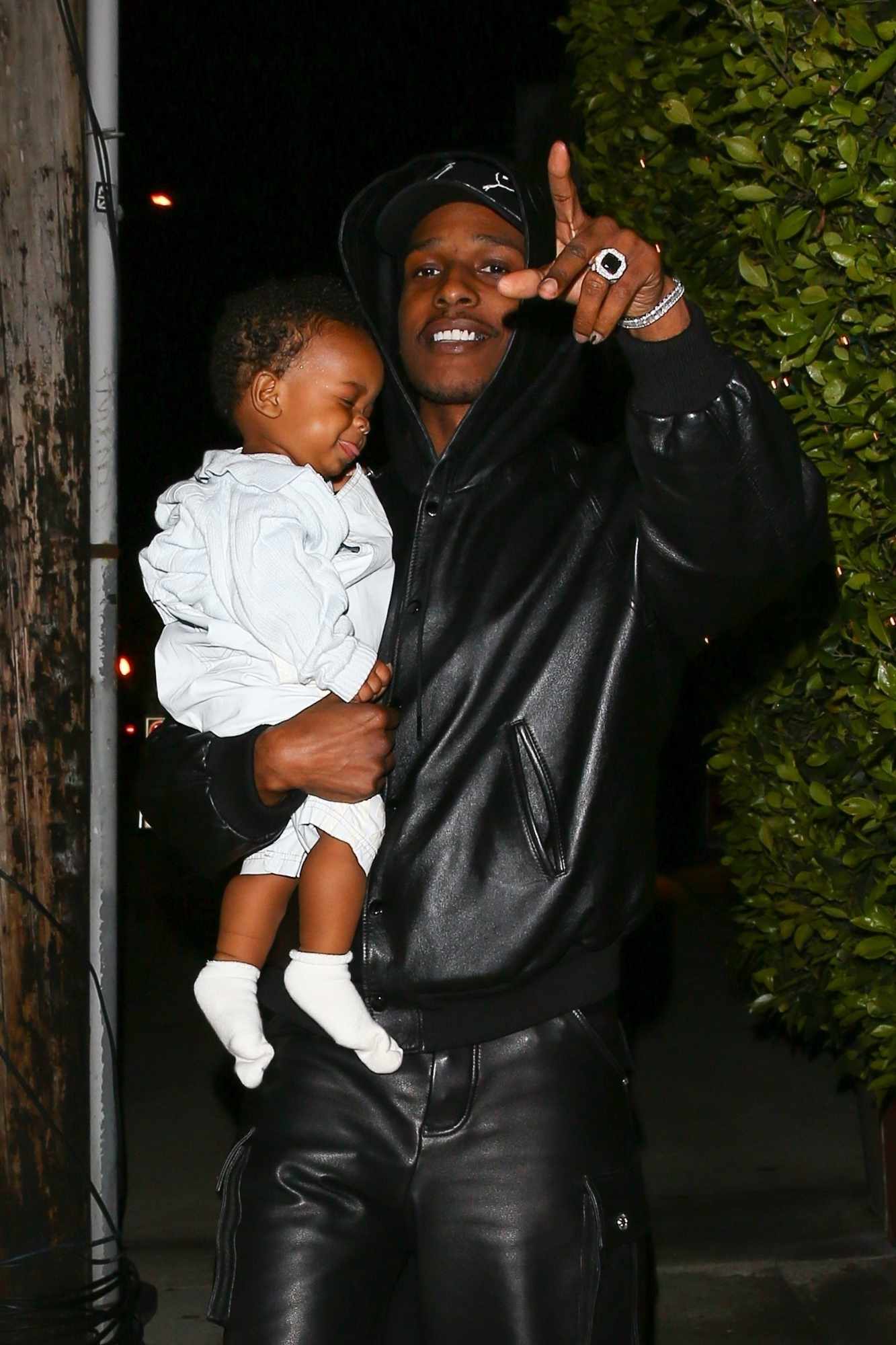 A$AP Rocky is seen wearing a black hoodie & PUMA hat holding his son RZA