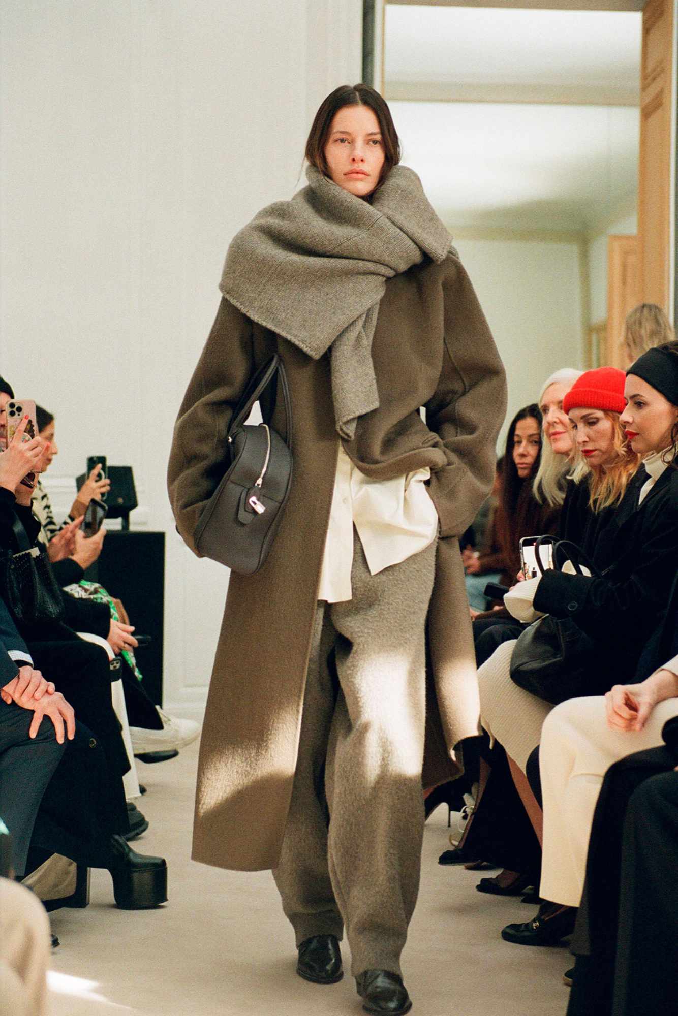 A model wears The Row's Fall/Winter 2023 collection, including a beige scarf, brown jacket, and white pants