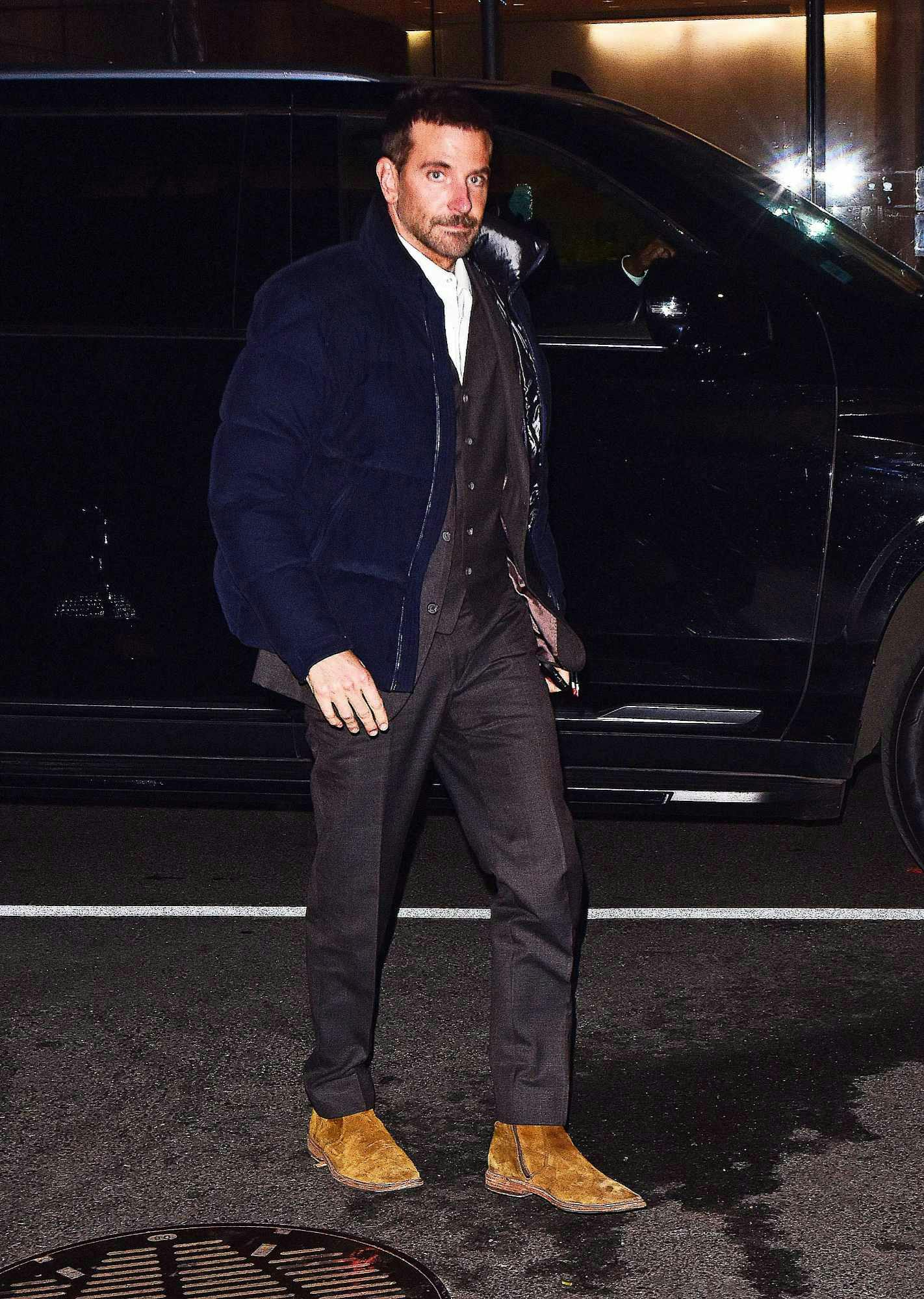 Bradley Cooper wears a Moncler puffer jacket over a brown suit in New York