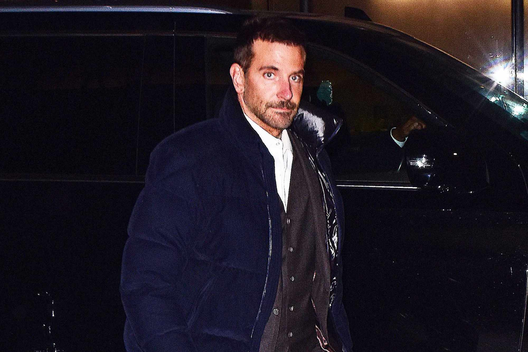 Bradley Cooper wears a Moncler puffer jacket over a brown suit in New York
