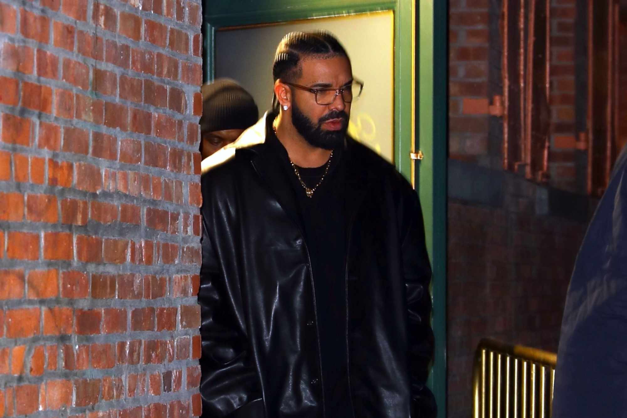 Drake wears a leather coat, black t-shirt, grey pants, and black leather shoes with glasses at Torrisi in New York