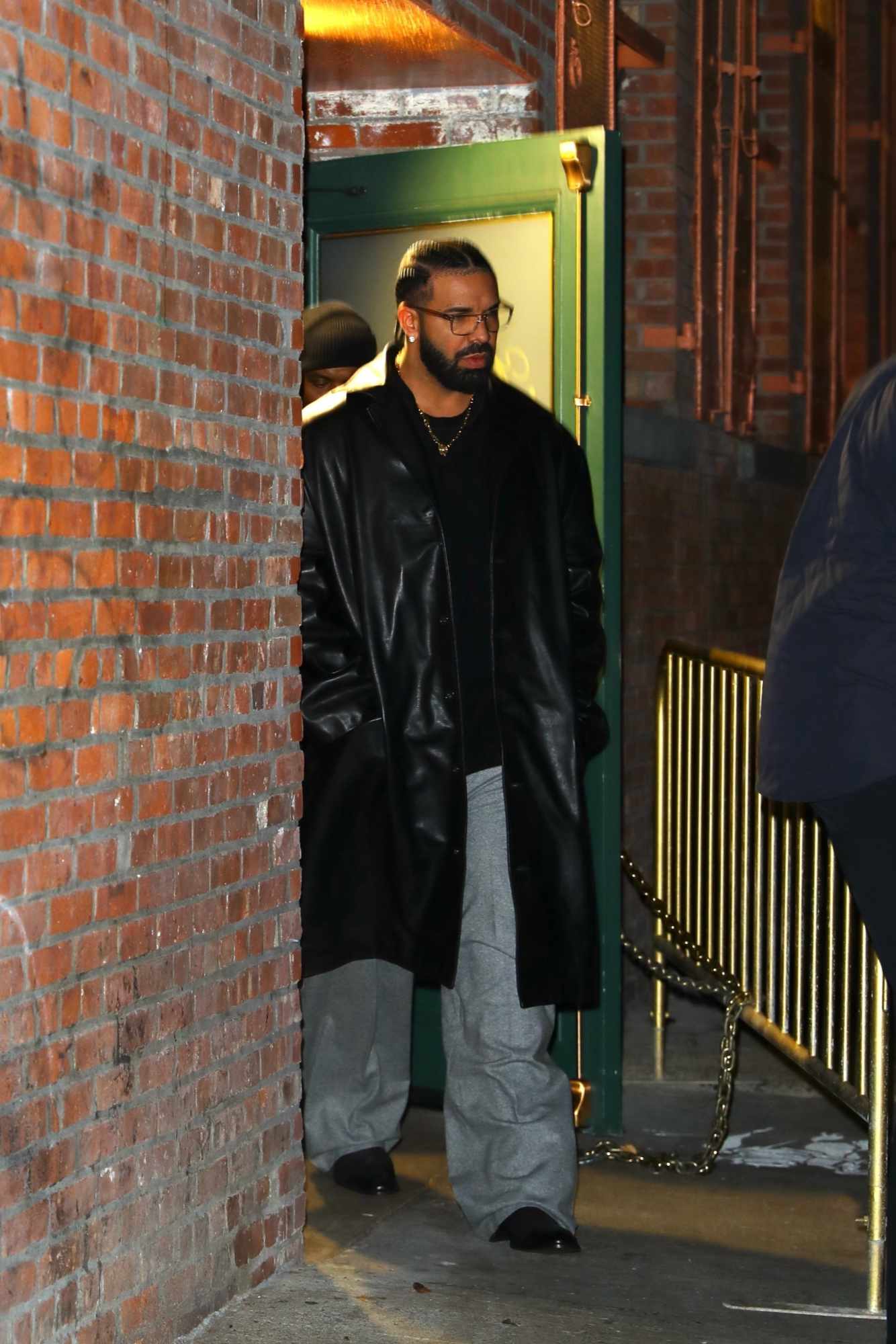 Drake wears a leather coat, black t-shirt, grey pants, and black leather shoes with glasses at Torrisi in New York