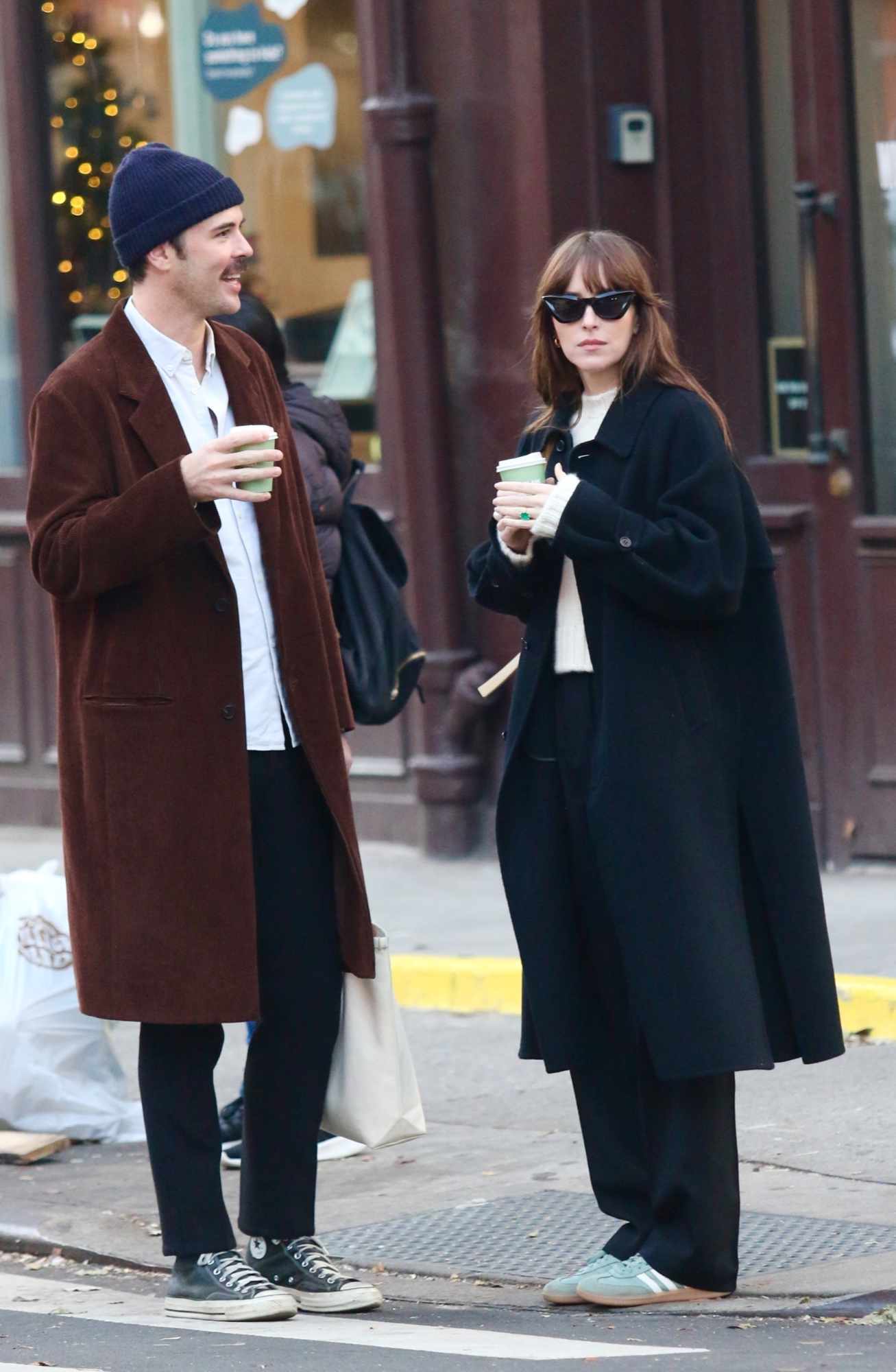 Dakota Johnson & Blake Lee wear oversized black coats & dark pants while drinking coffee in New York