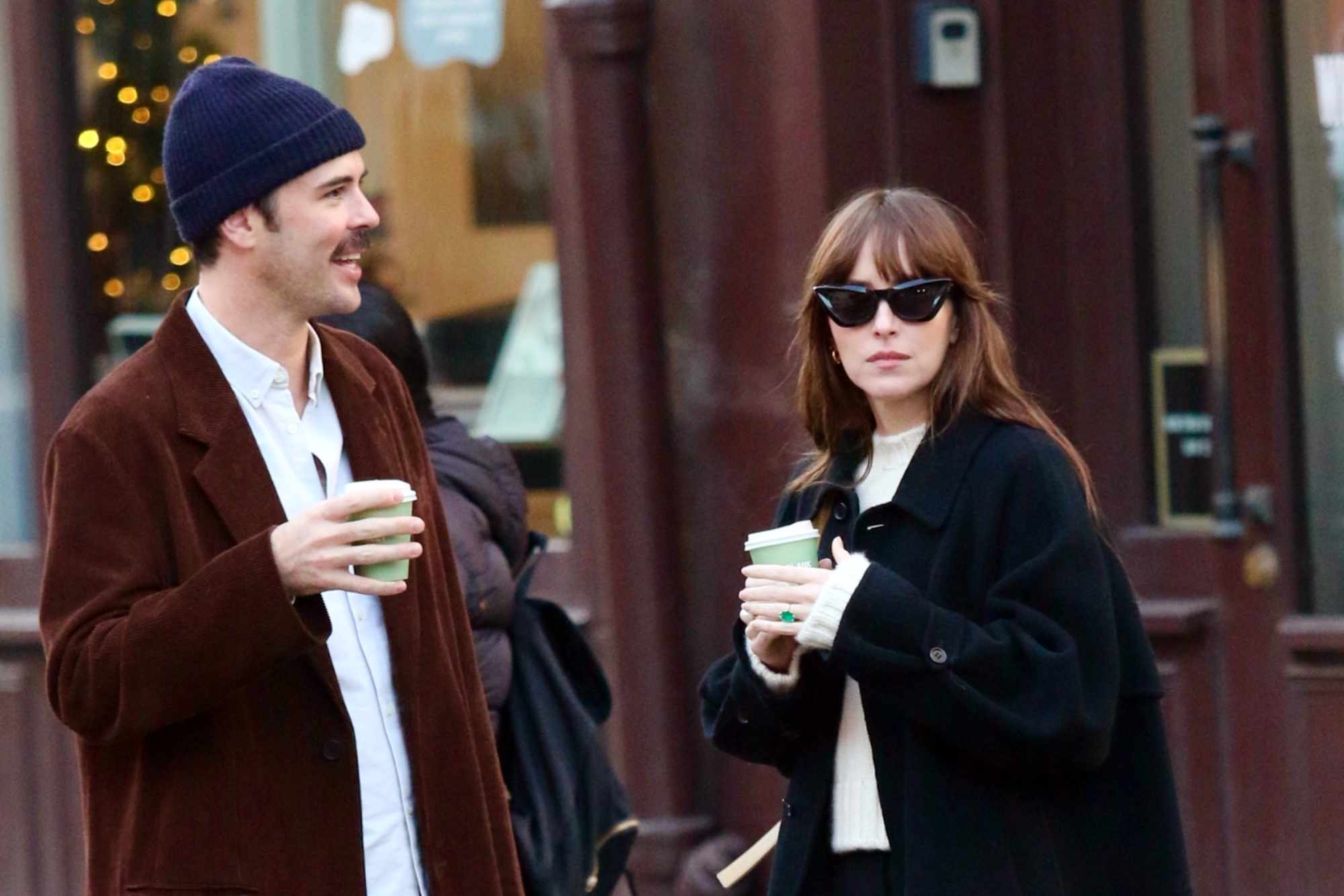 Dakota Johnson & Blake Lee wear oversized black coats & dark pants while drinking coffee in New York