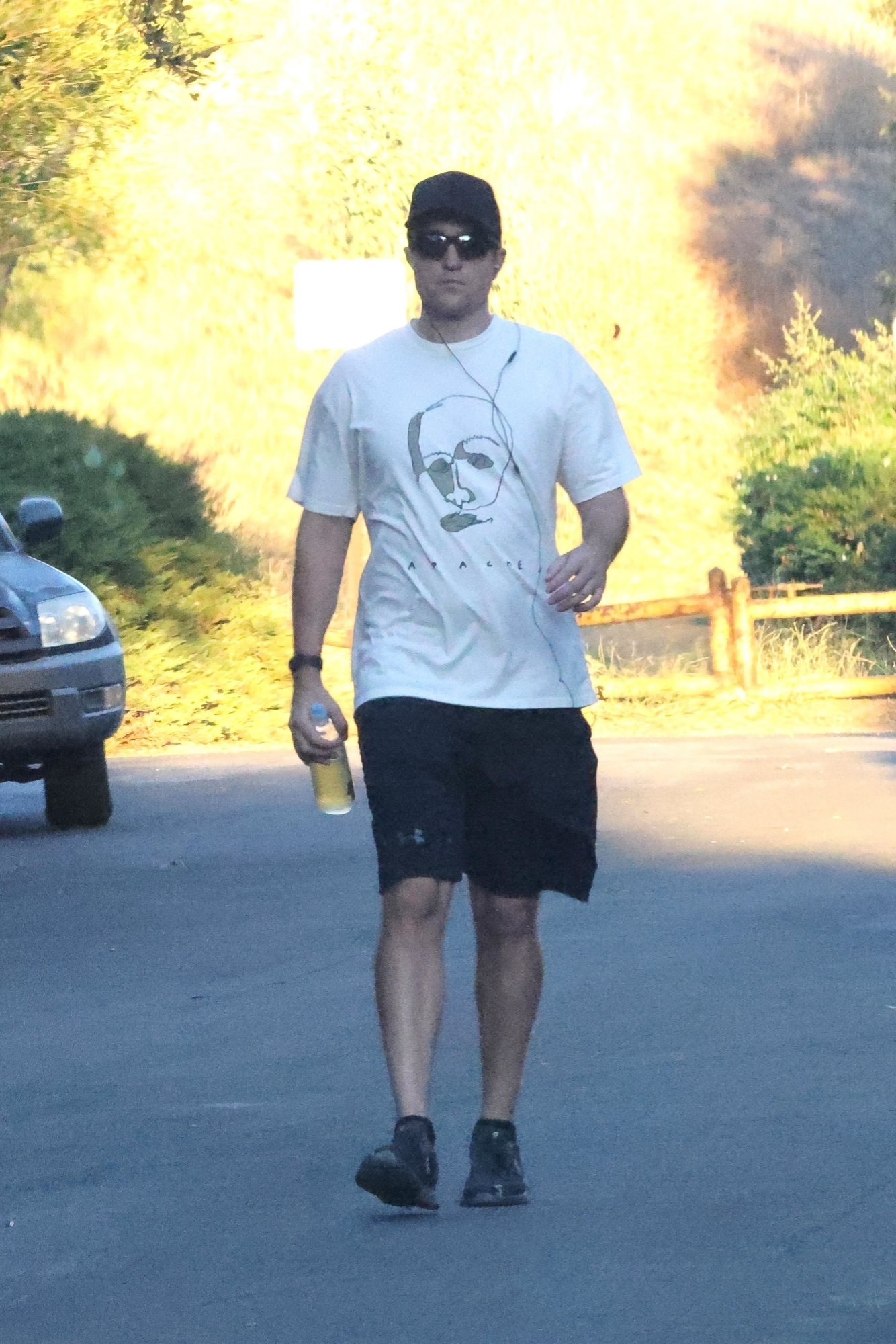 Robert Pattinson wears a black hat, white T-shirt, black shorts, and black shoes
