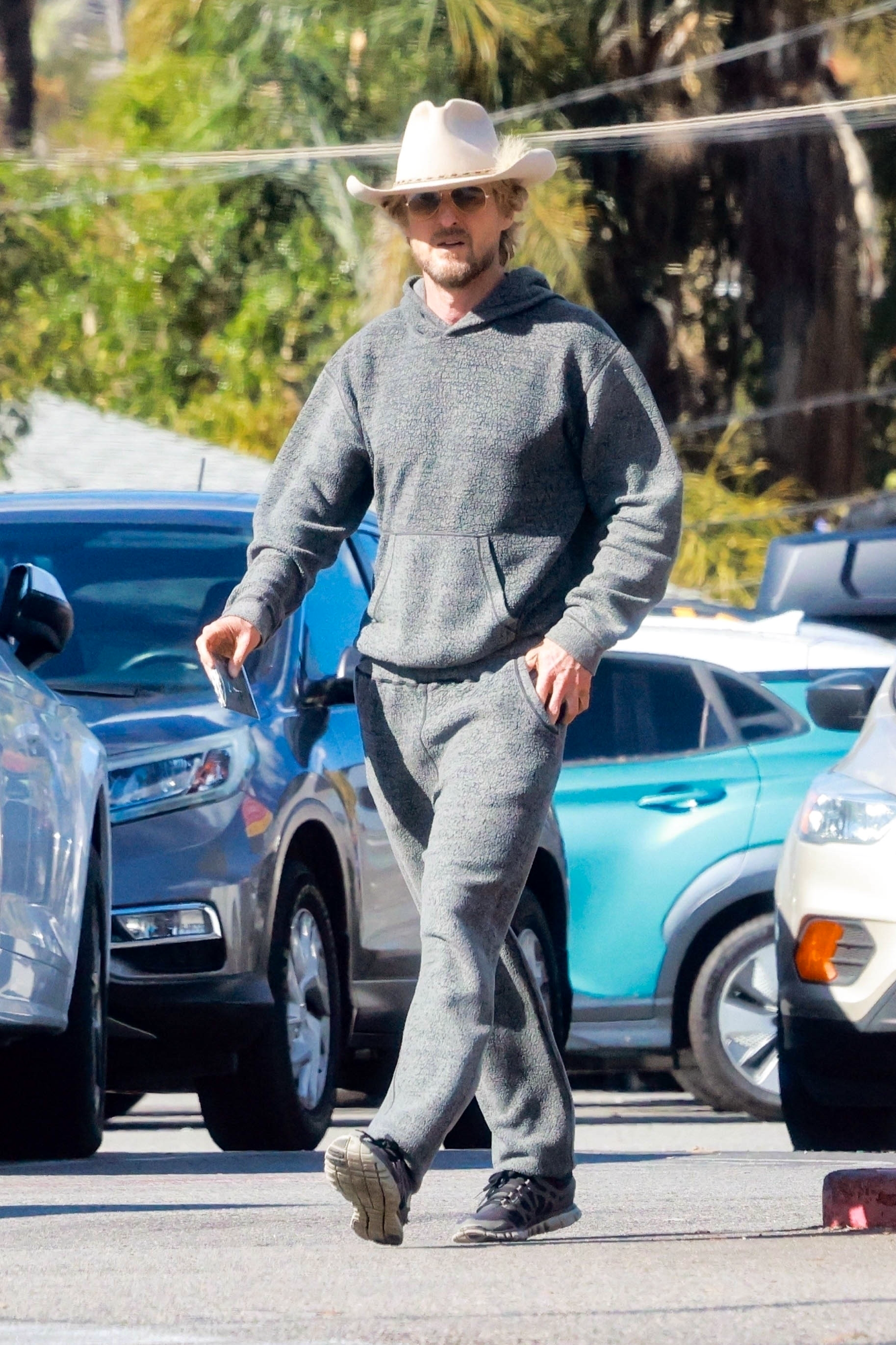 Owen Wilson seen wearing a white cowboy hat with feather & grey sweatsuit with Nike running sneakers
