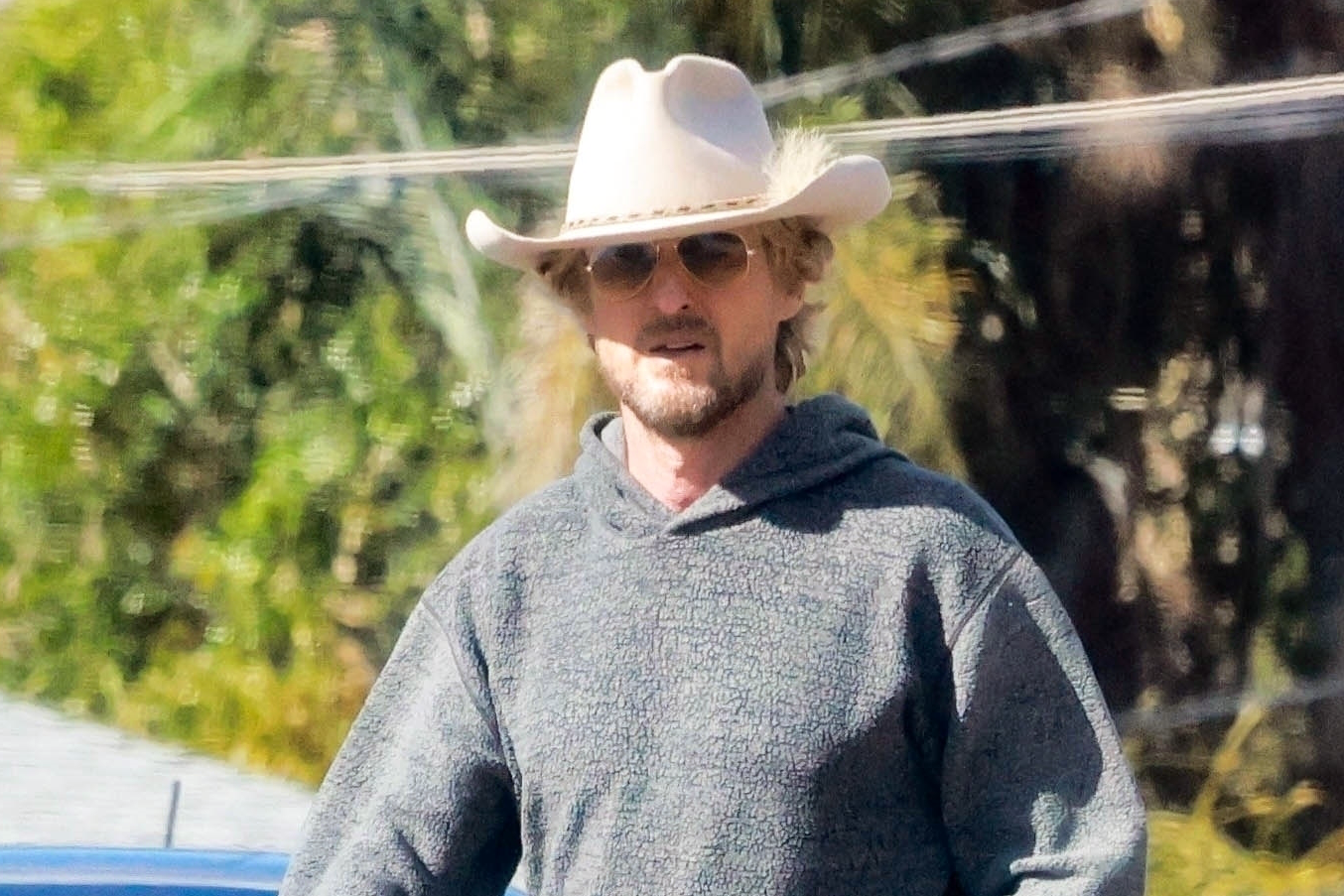 Owen Wilson seen wearing a white cowboy hat with feather & grey sweatsuit with Nike running sneakers