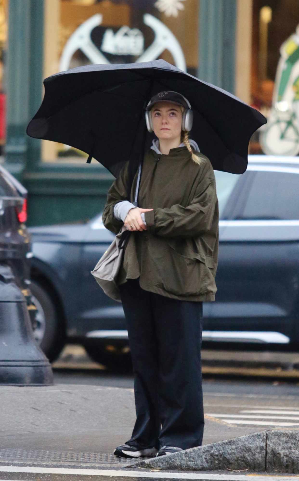 Singer Lorde seen standing in the rain with an umbrella, green jacket & navy pants