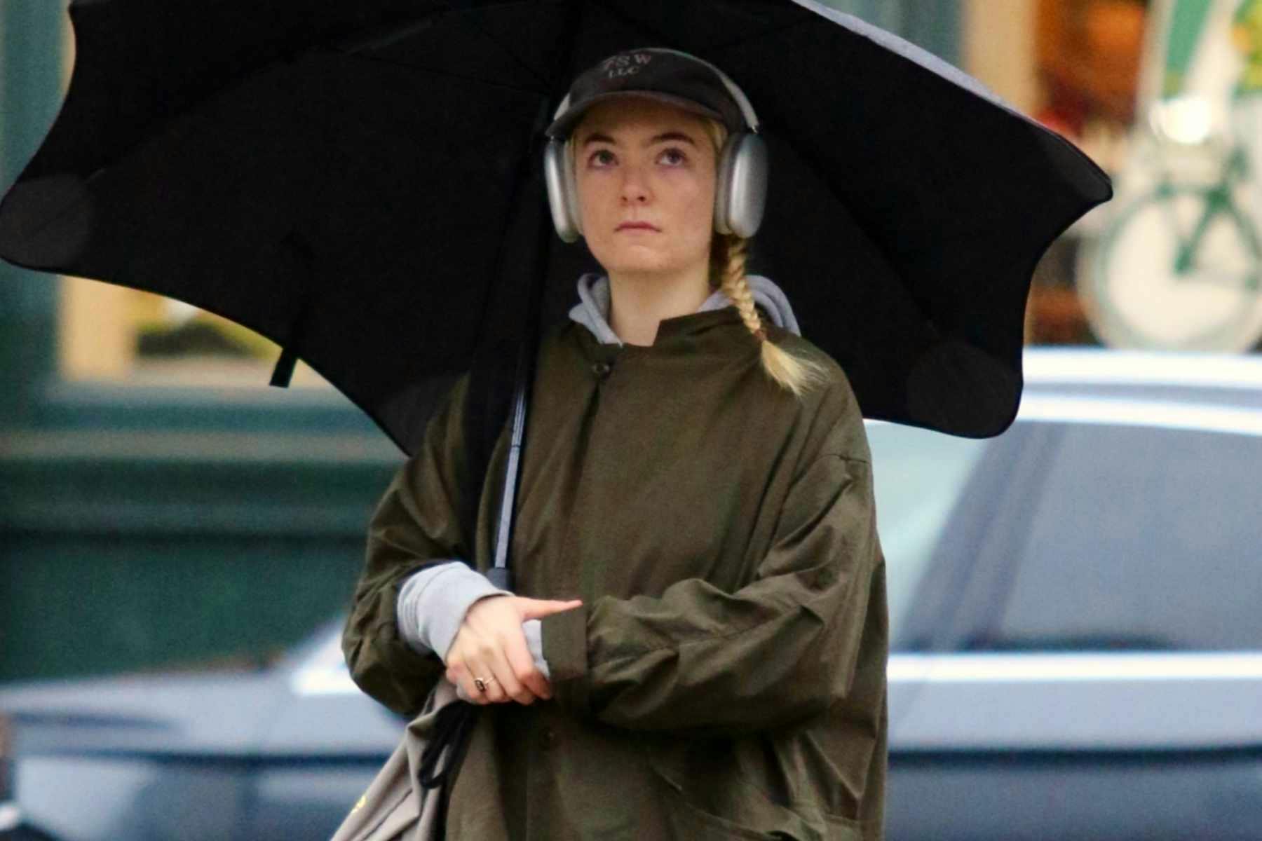 Singer Lorde seen standing in the rain with an umbrella, green jacket & navy pants