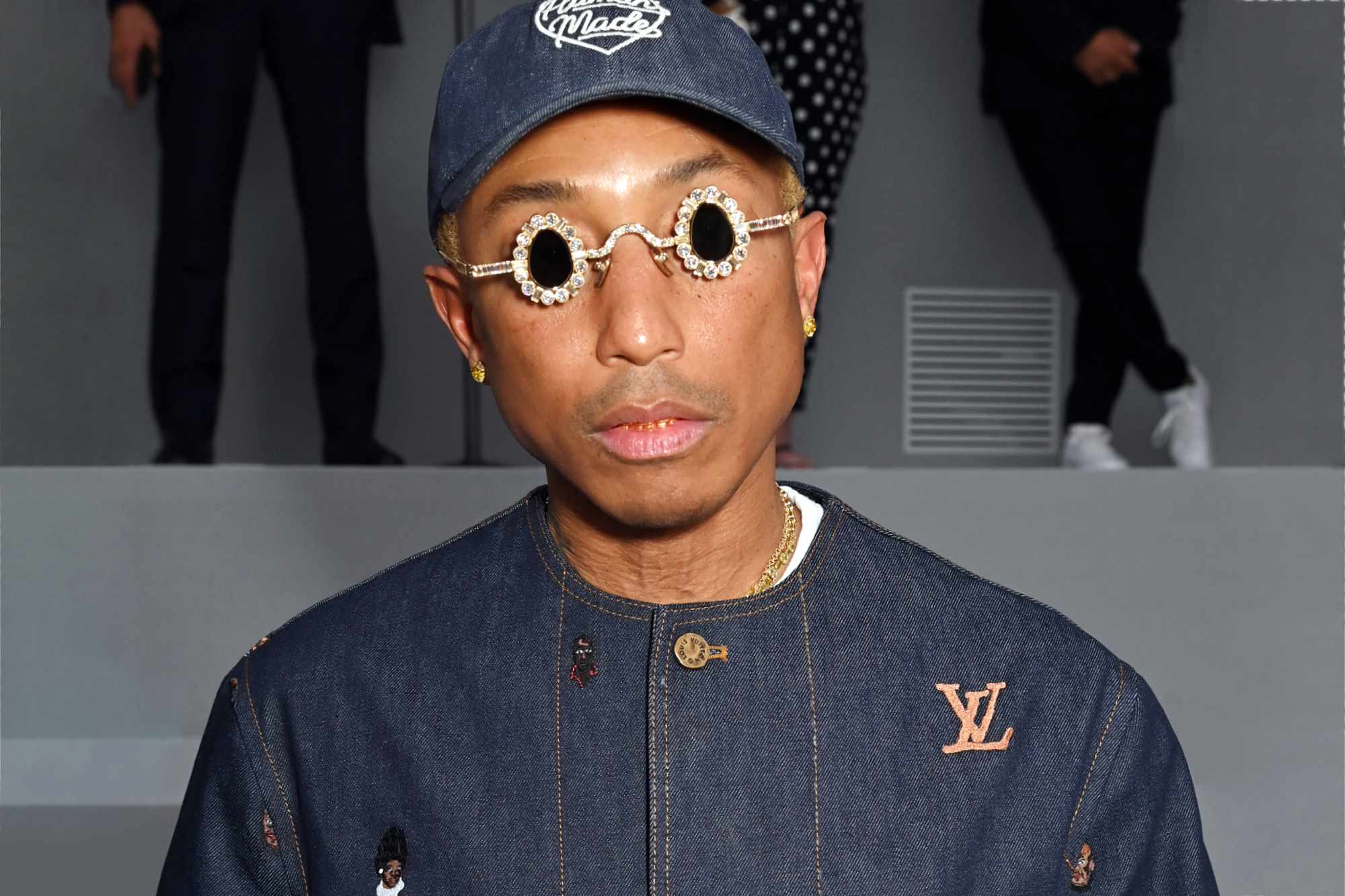 Pharrell Williams wears a Human Made hat, Tiffany sunglasses & a denim Louis Vuitton shirt