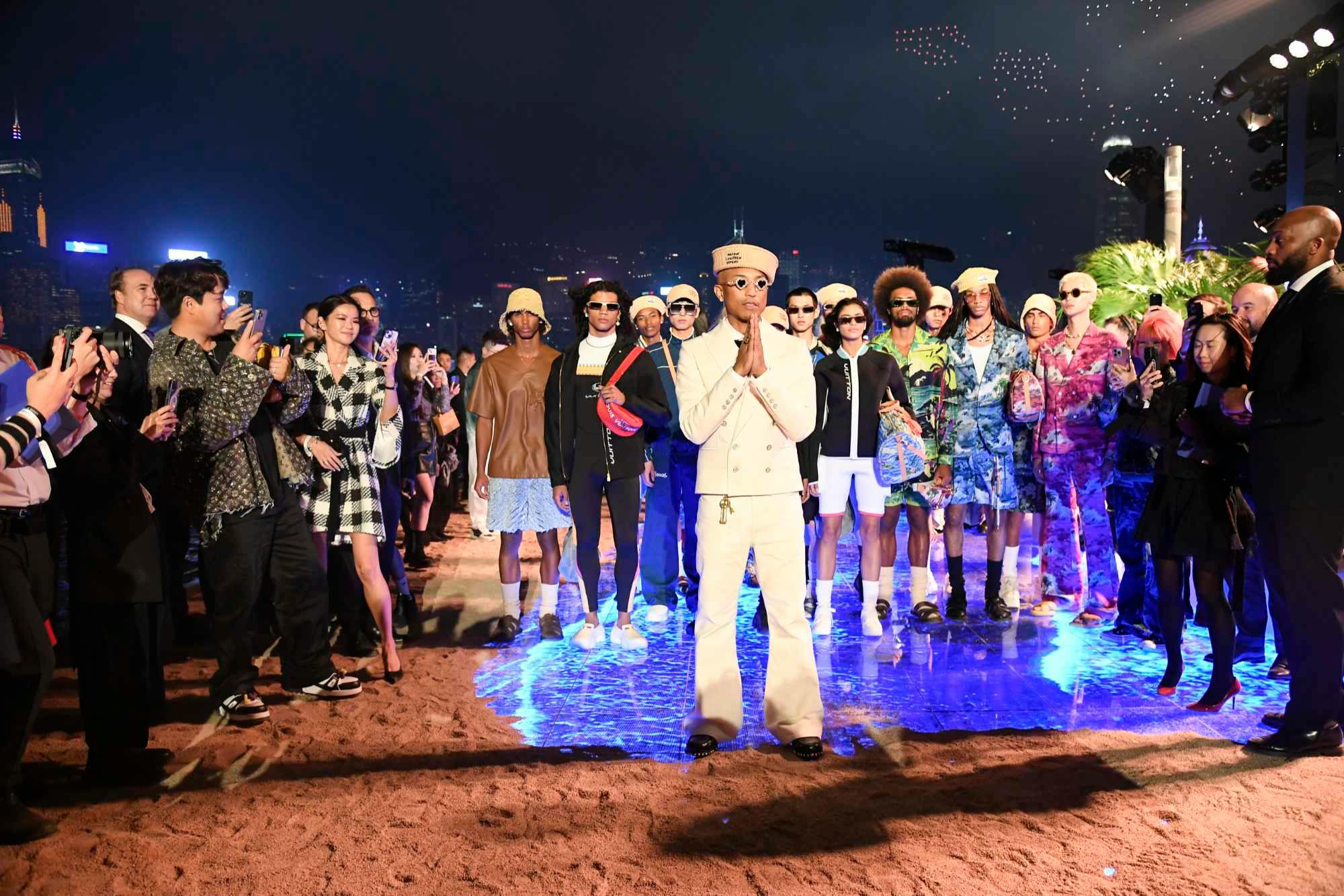 Pharrell Williams wearing a white suit and Tiffany sunglasses stands in front of models on the Louis Vuitton Pre-Fall 2024 runway in Hong Kong